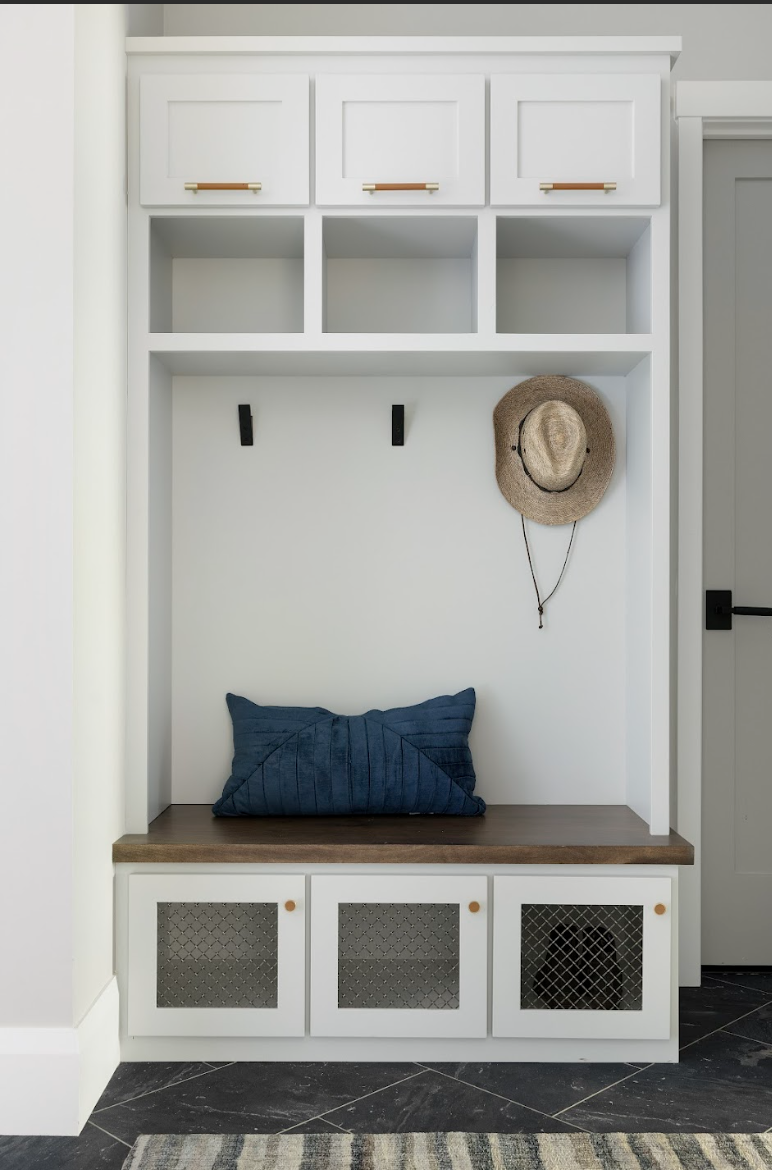 Custom mudroom built-in with white cabinetry, bench seating, upper cubbies, brass hardware, and concealed storage