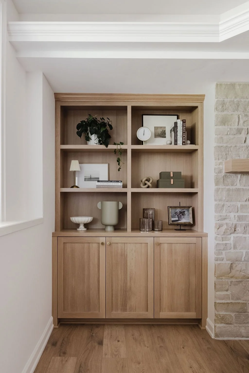 Warm wood built-in shelving unit with curated decor, set against white walls and adjacent stone detail.
