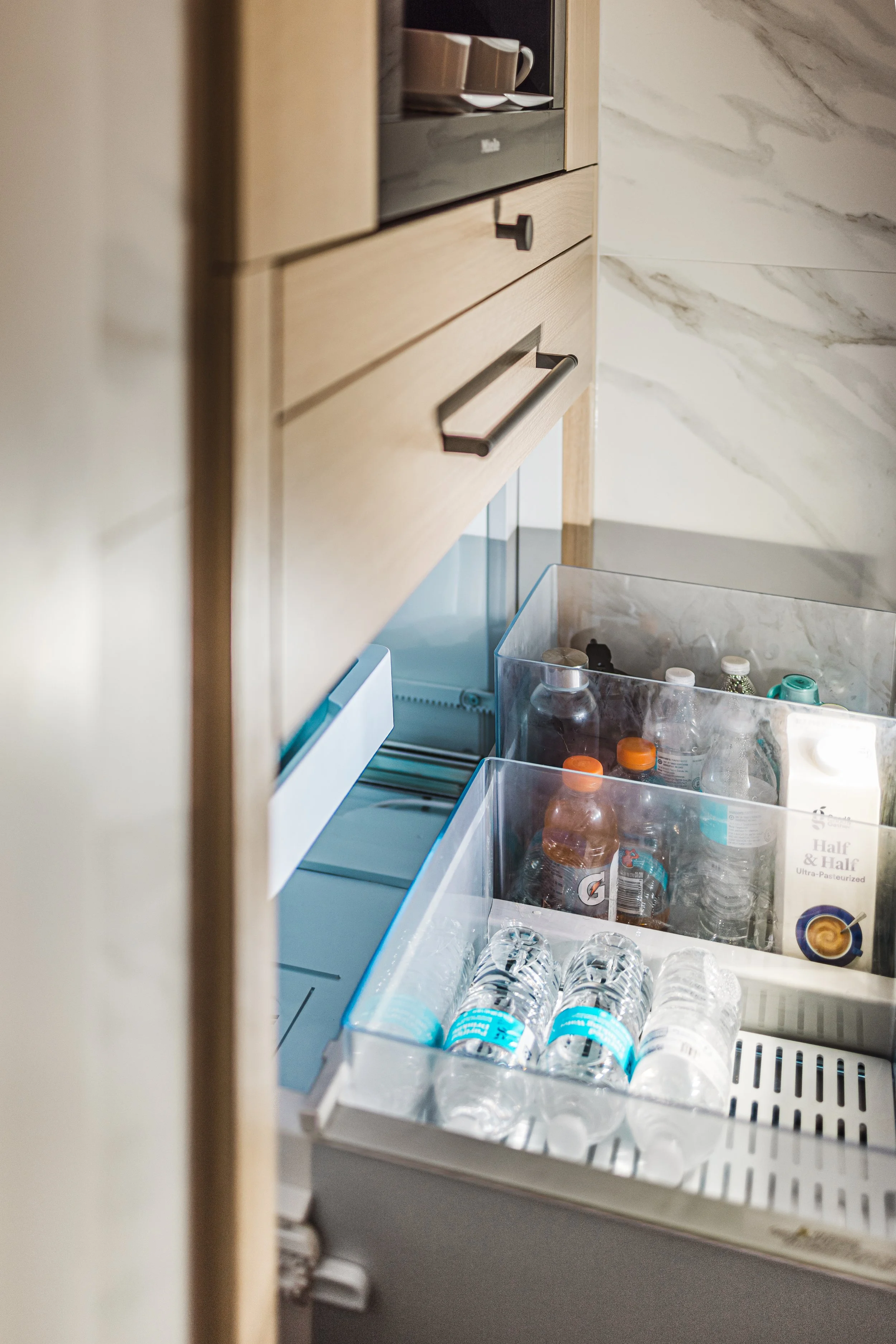 Modern wood cabinets with open refrigerated drawer organized with water bottles and beverages.