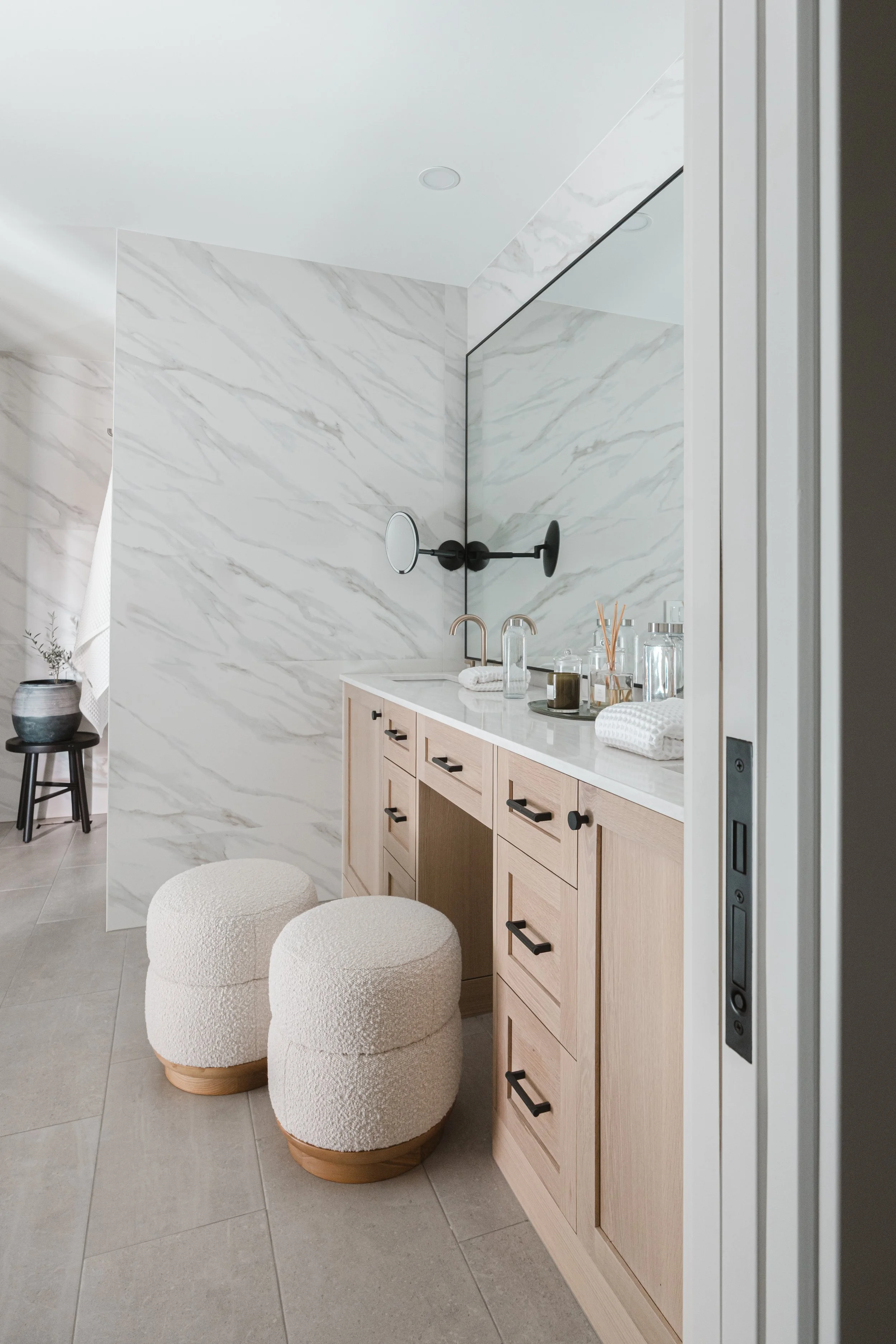 Close-up of light wood bathroom cabinets with makeup vanity, marble backsplash, and dual mirrors