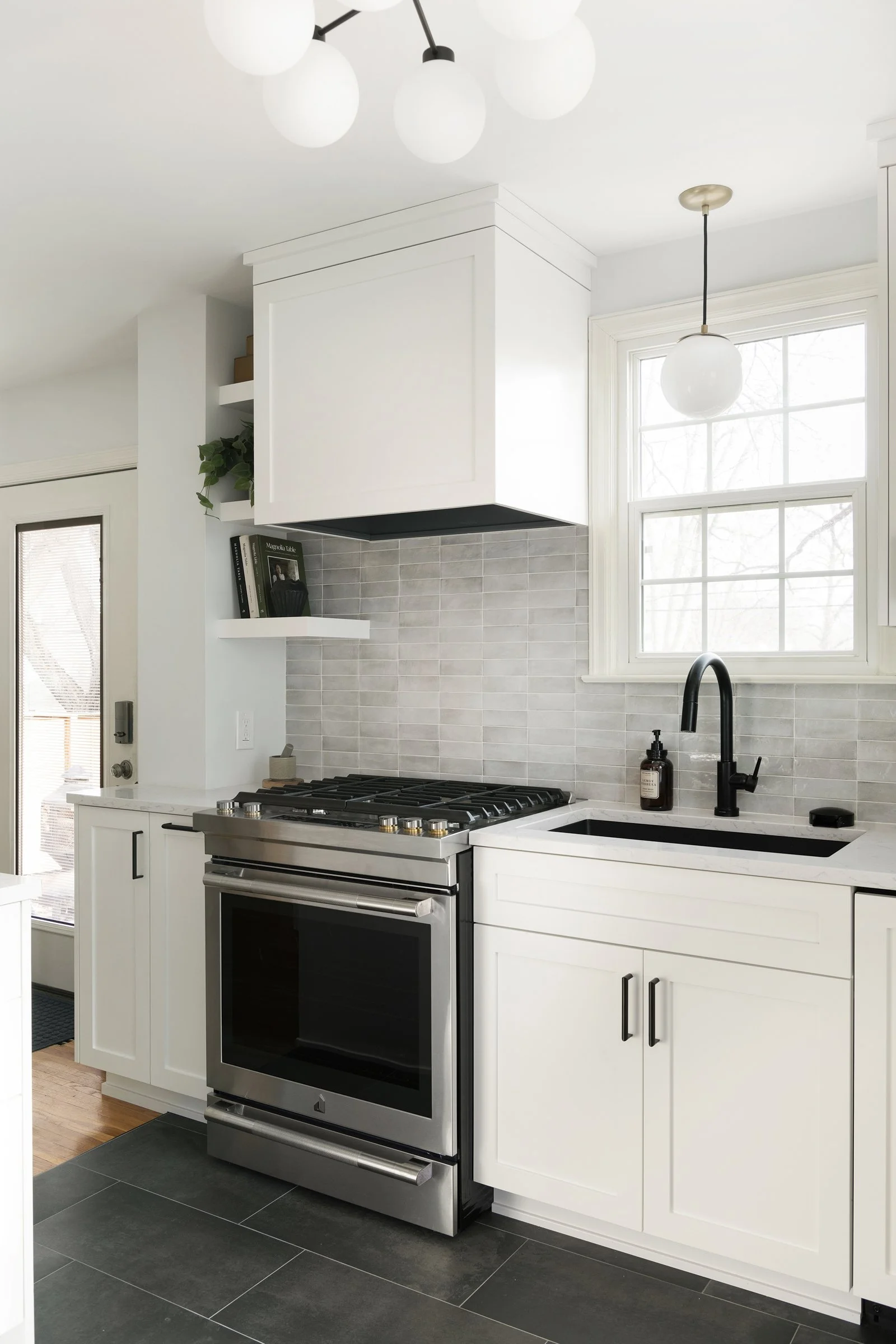 White shaker cabinets with black hardware in a bright kitchen with a gas range and tiled backsplash