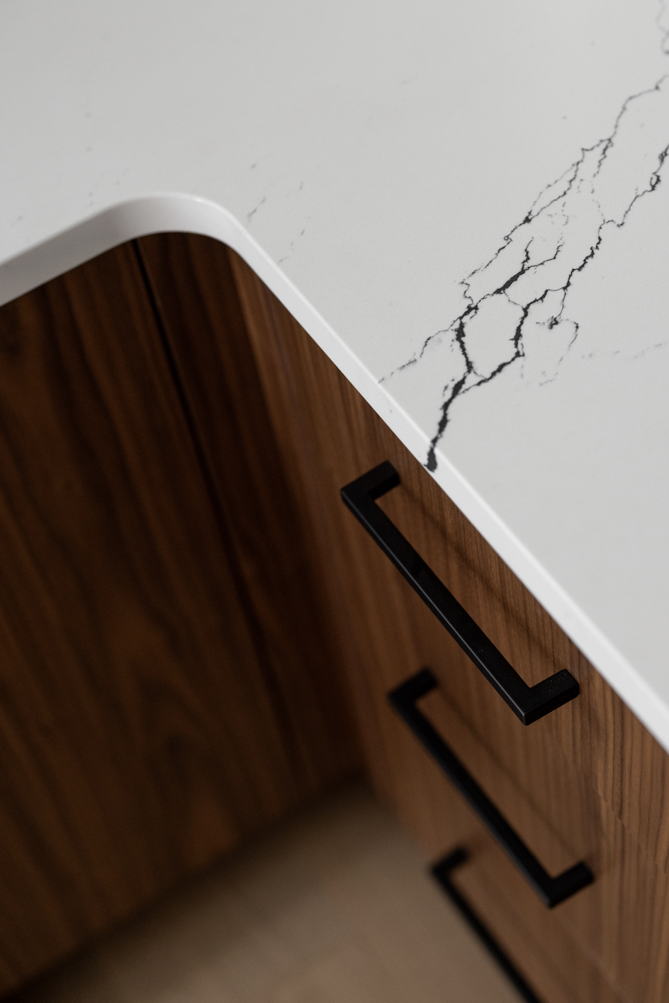 Precision-focused detail of a custom kitchen corner featuring walnut slab-style drawers and high-contrast white quartz countertops with black marble-style veining. The shot highlights the seamless grain alignment and the sleek integration of minimali