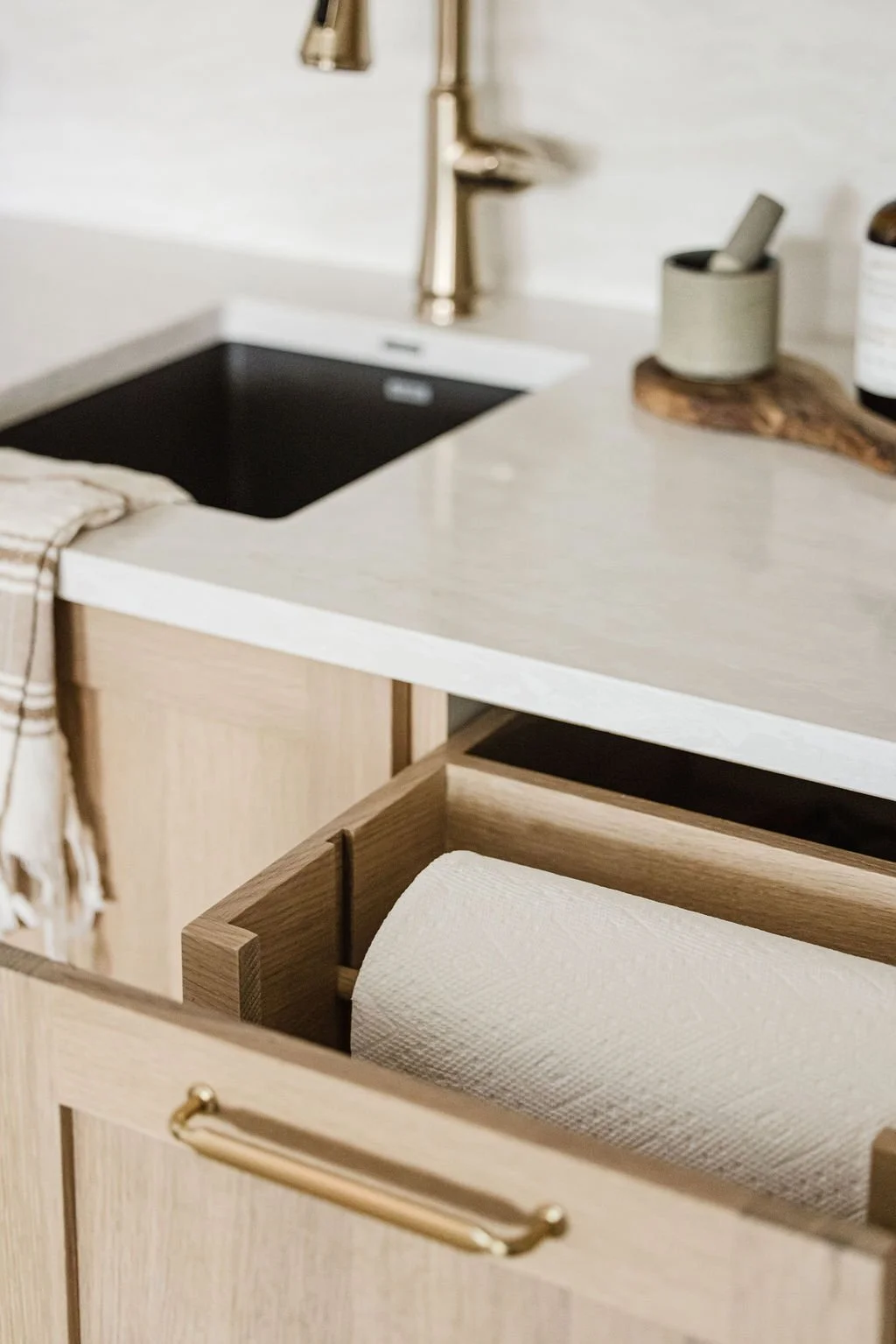 Light wood cabinet drawer with integrated paper towel holder, paired with a white countertop and brass faucet