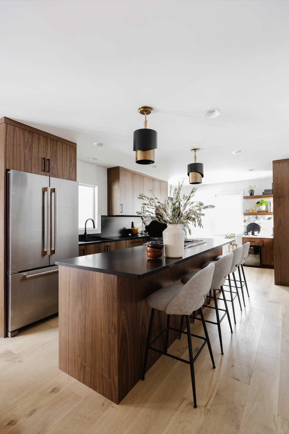 Contemporary kitchen with floor-to-ceiling walnut cabinets, black waterfall island countertop, upholstered bar stools, and brass-accent pendant lights.