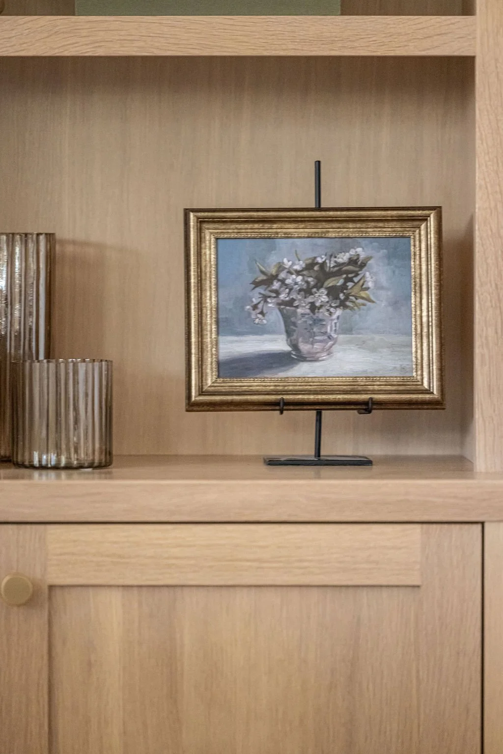 Styled wood shelving with framed floral art and textured glass decor in a warm, minimalist display.