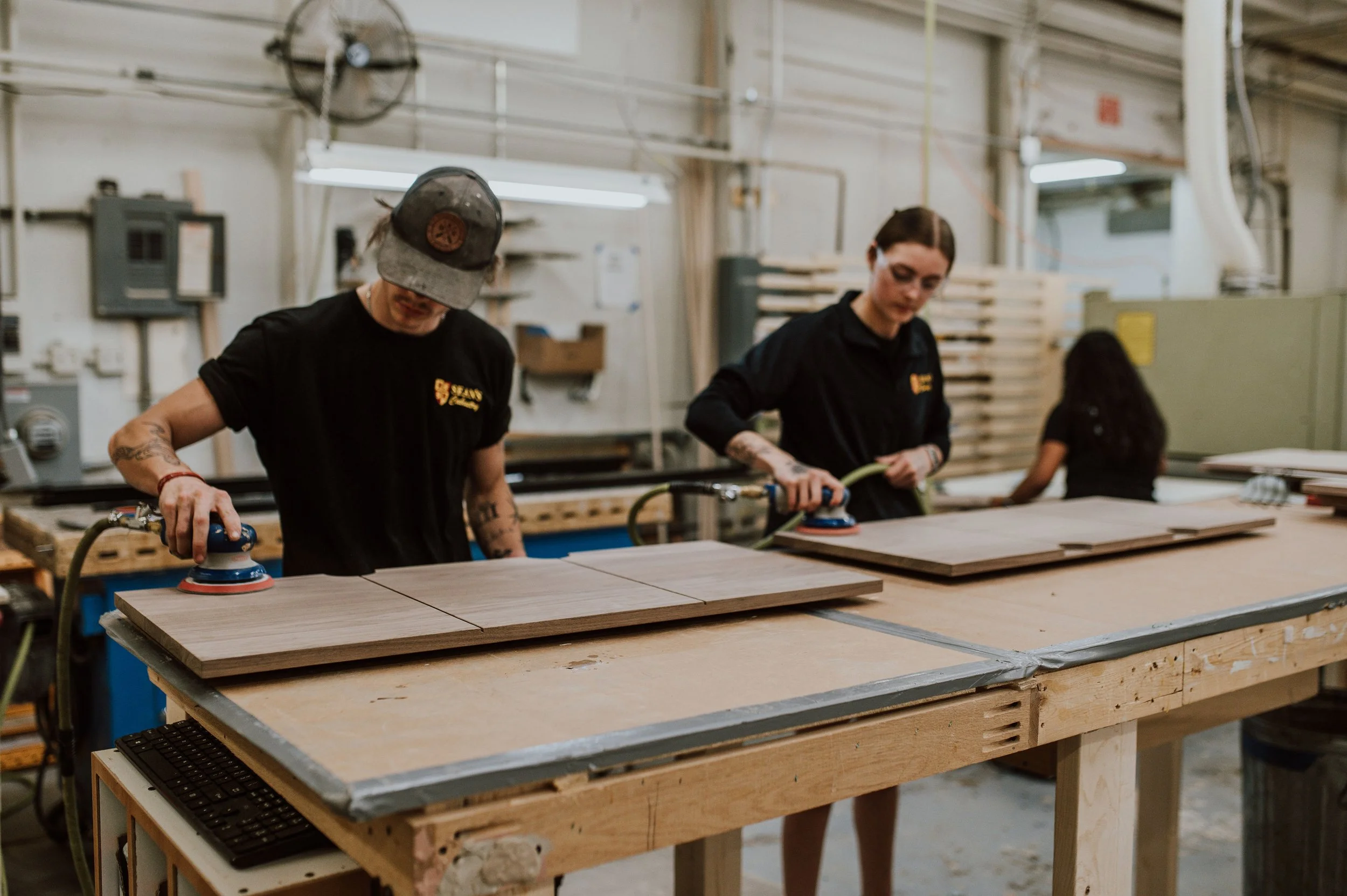 Team members sanding custom cabinet panels in workshop