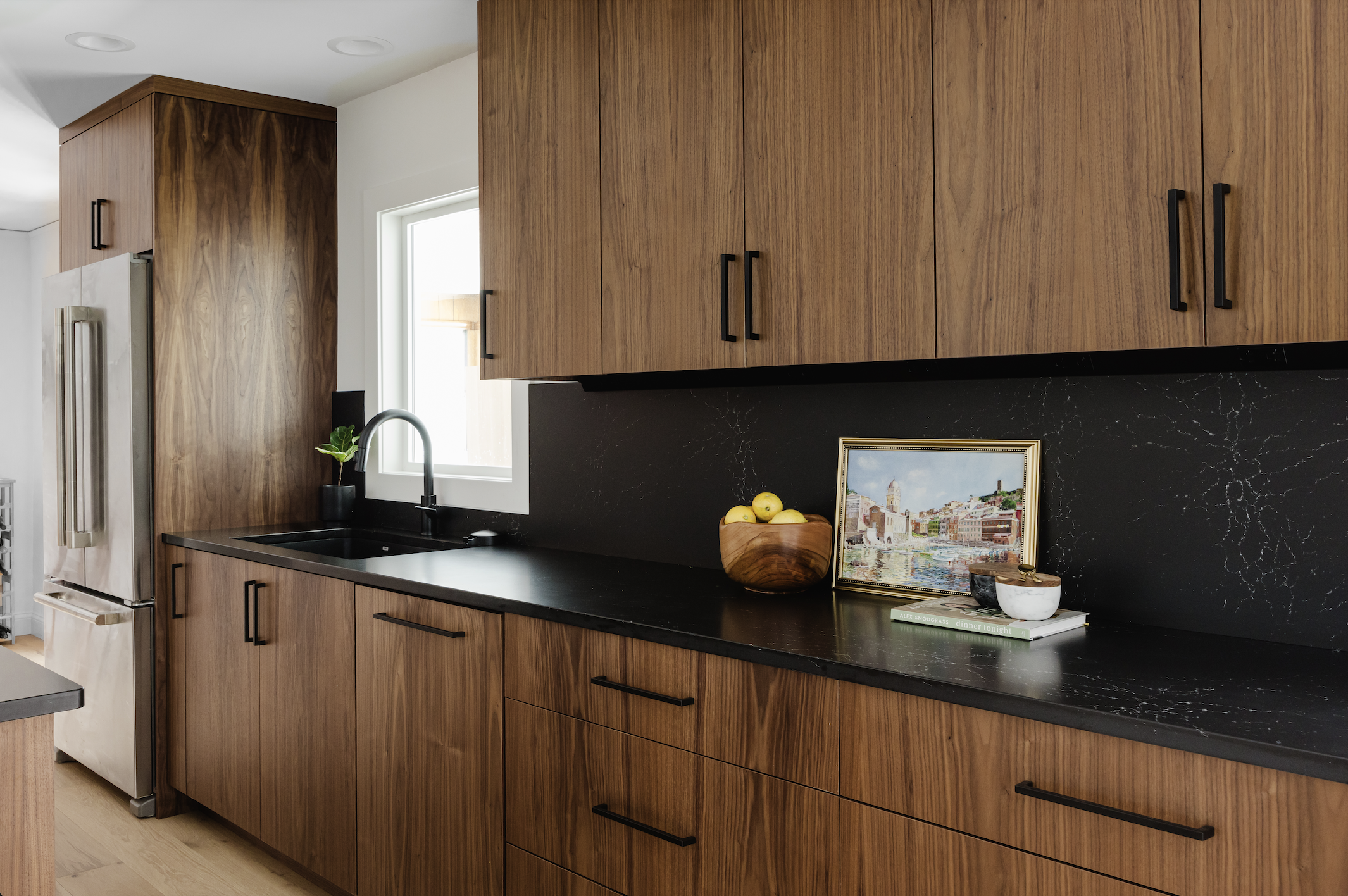 Custom walnut kitchen island with black countertops and flat-panel drawers, featuring modern black and gold pendant lights and large-scale framed line art on a white wall.
