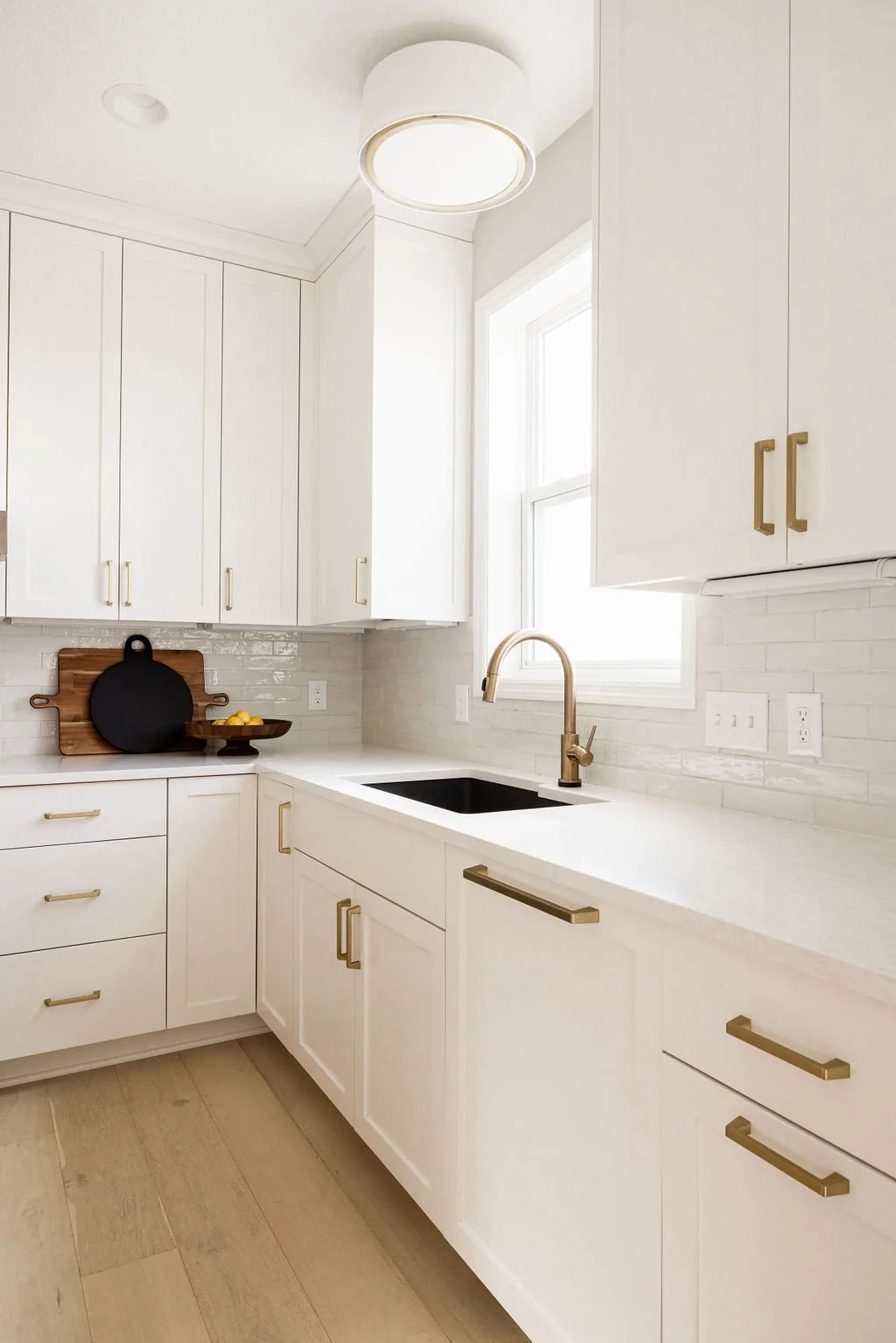 Custom white kitchen cabinets with gold handles, quartz countertops, and a black undermount sink set against a light tile backsplash.