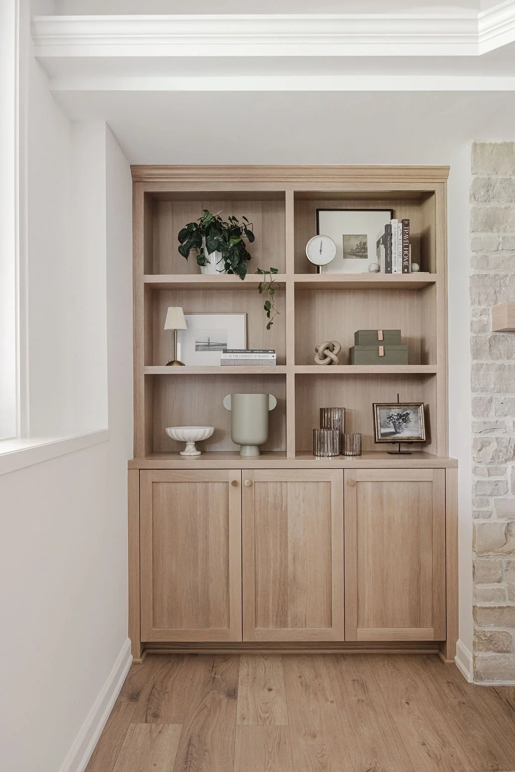 Light oak built-in cabinetry with open display shelves and lower cabinet storage, styled with decor.