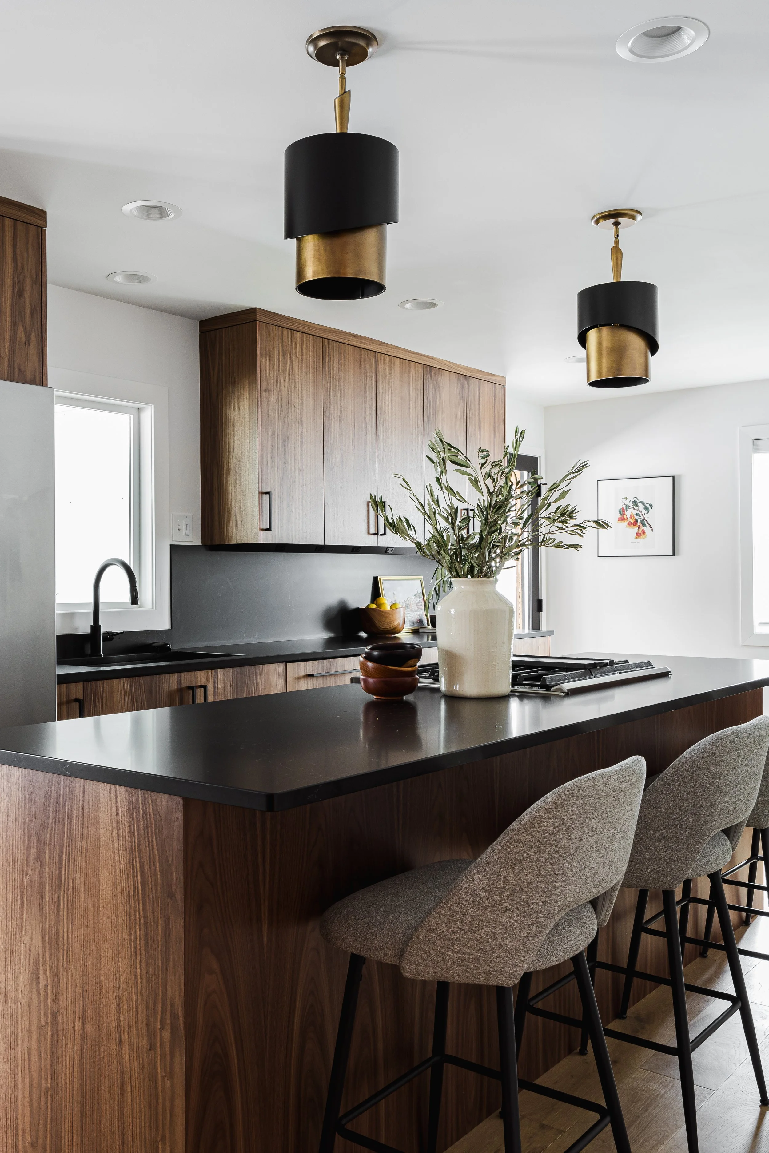 Custom walnut kitchen island with gray seating and black stone countertops. This modern kitchen design showcases flat-panel wood cabinets with a continuous vertical grain, integrated appliances, and minimalist black hardware.