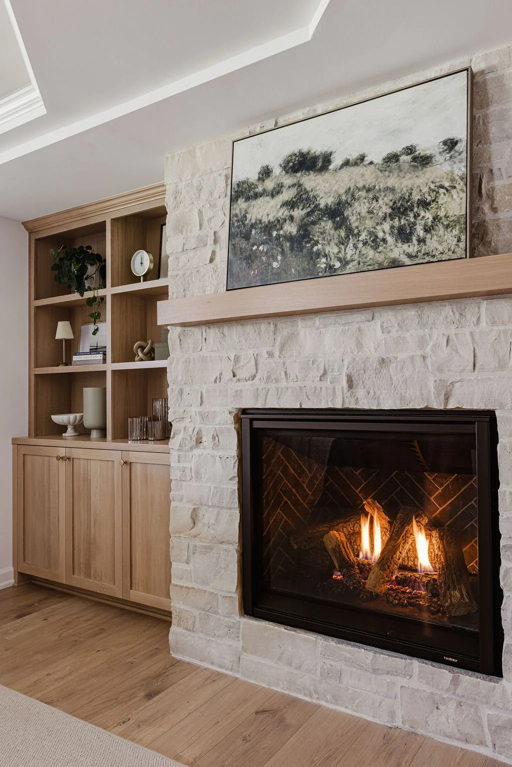 Custom light wood built-in cabinetry with open shelves and lower storage, paired with a white stone fireplace, wood mantel, and modern gas insert in a warm contemporary living room