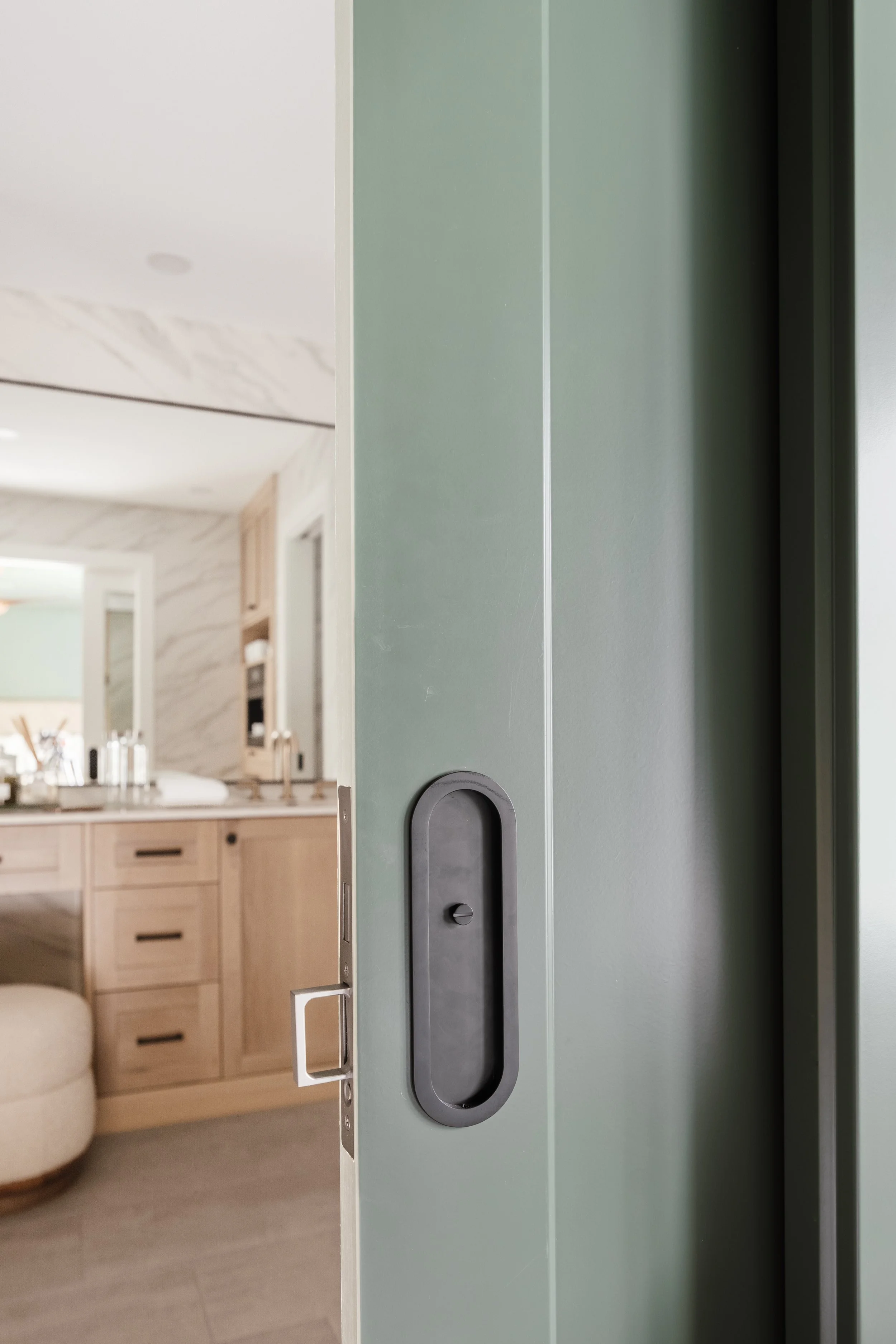 Soft green sliding door partially open revealing custom wood cabinets and a modern vanity in the background
