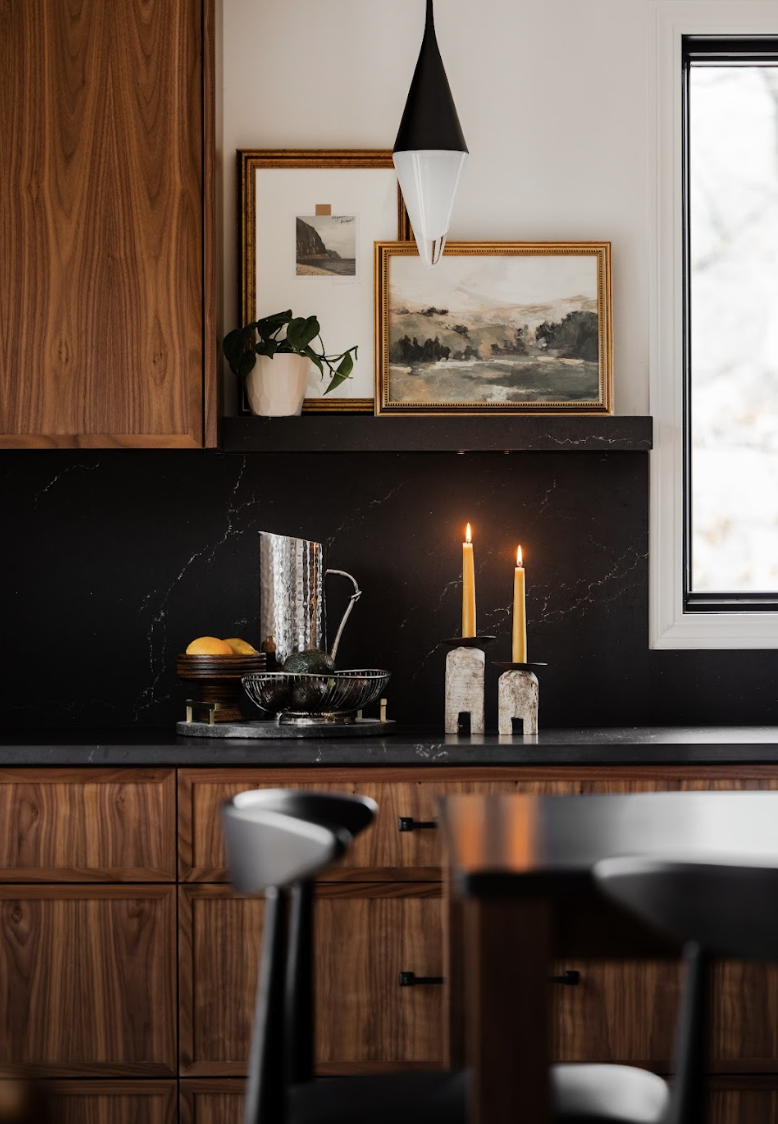 Custom walnut cabinets in a modern kitchen with black quartz backsplash, styled with artwork, warm lighting, and curated countertop accessories