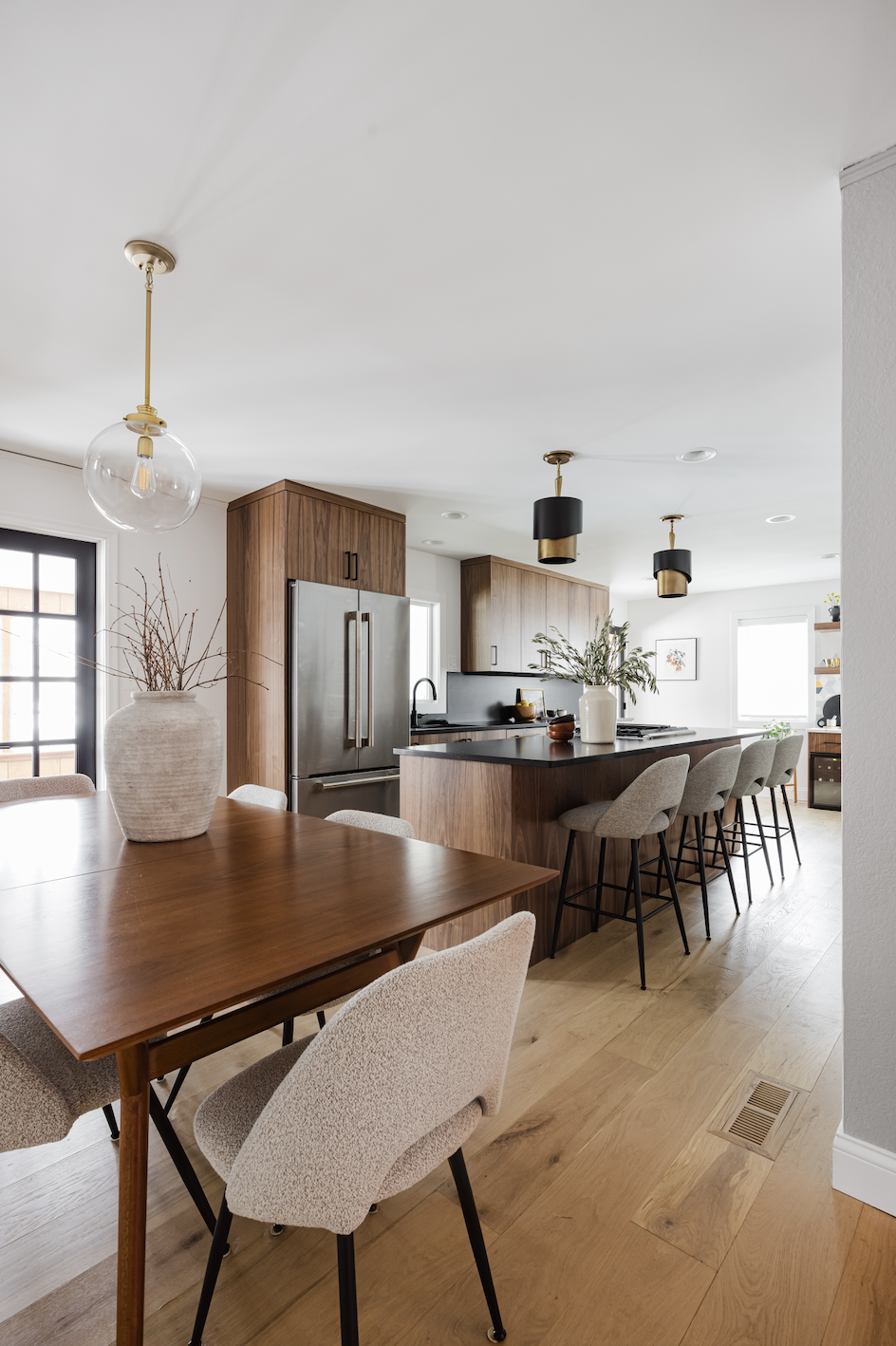 Open-concept kitchen and dining area featuring walnut cabinetry, a large island with seating, stainless steel appliances, and light wood flooring.