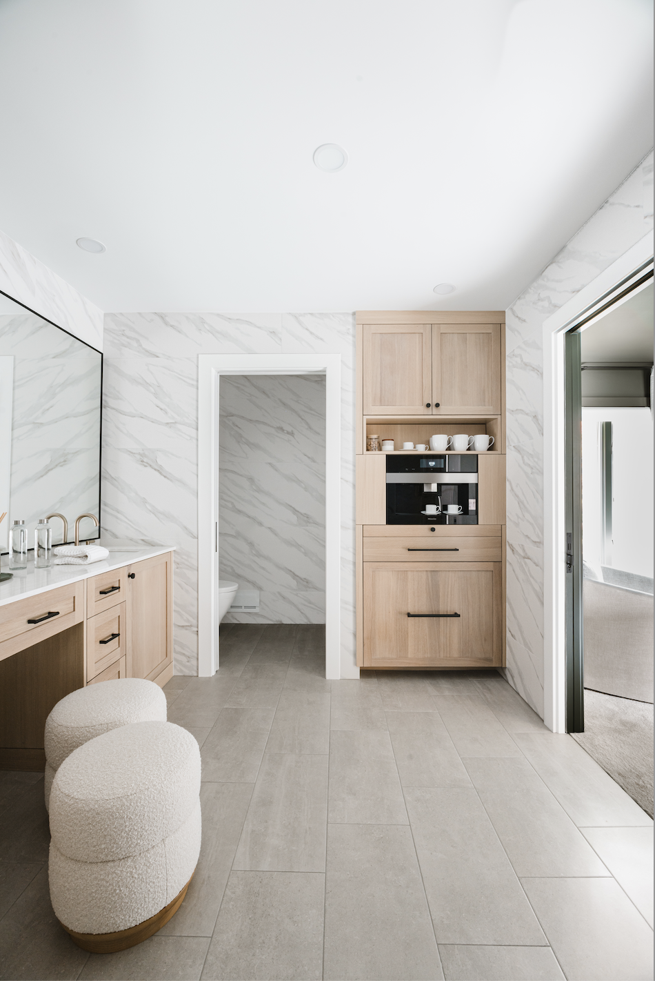 Modern bathroom with built-in light wood cabinets, makeup vanity, and marble wall surround
