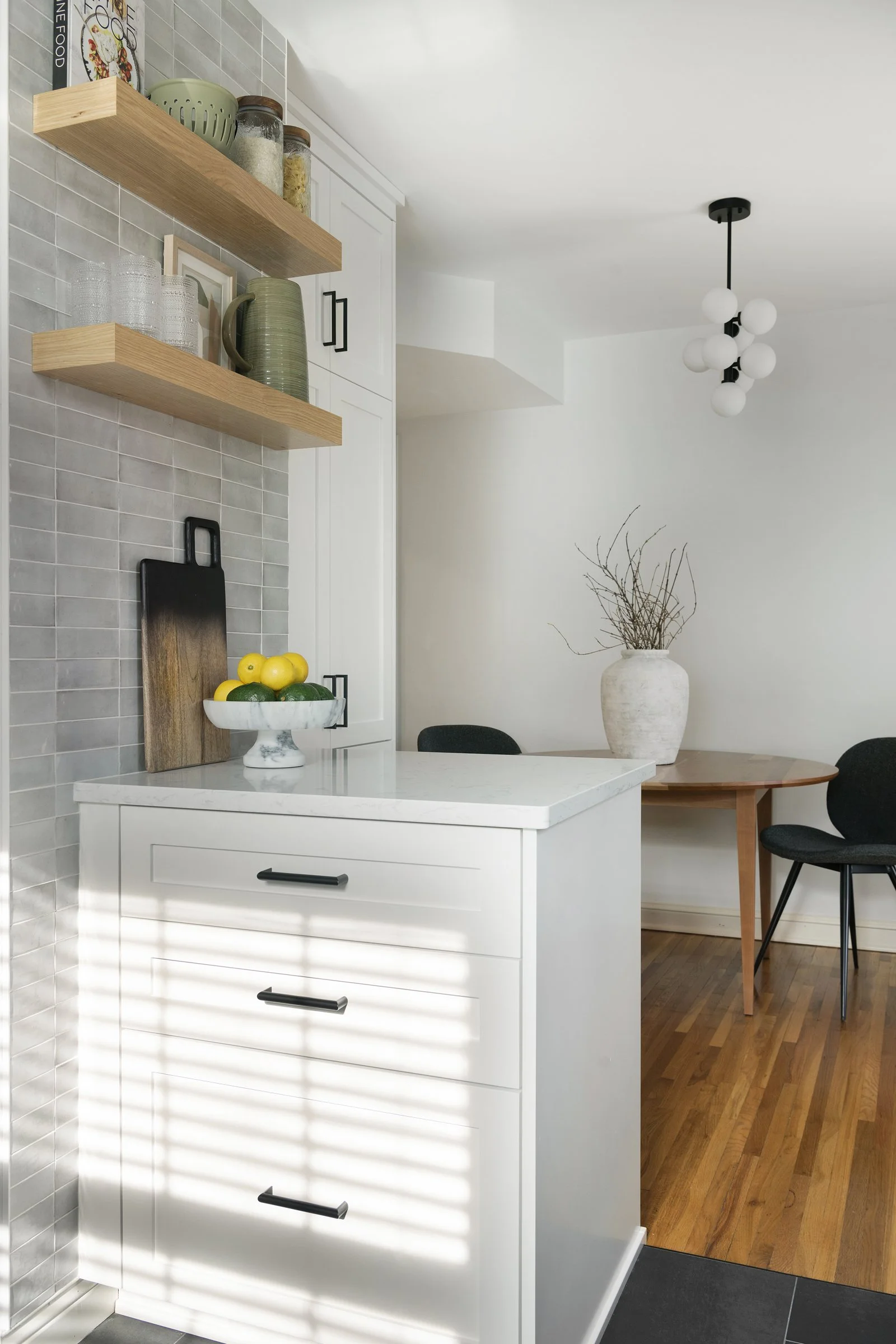 White custom drawer cabinets with black hardware, natural wood floating shelves, and a marble countertop