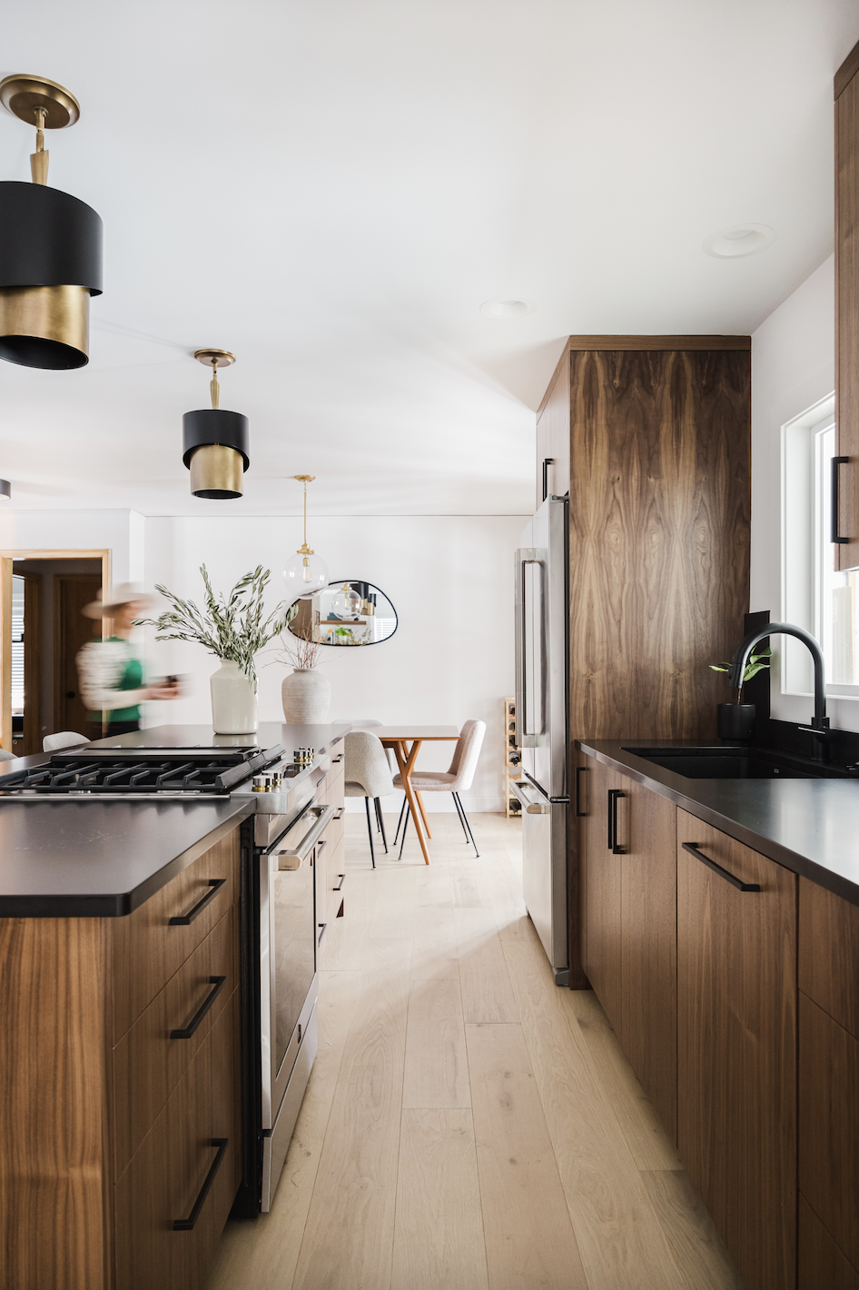Wide view of custom walnut kitchen cabinetry featuring integrated appliance panels, a black undermount sink, and a long wood-paneled island with a built-in gas range.