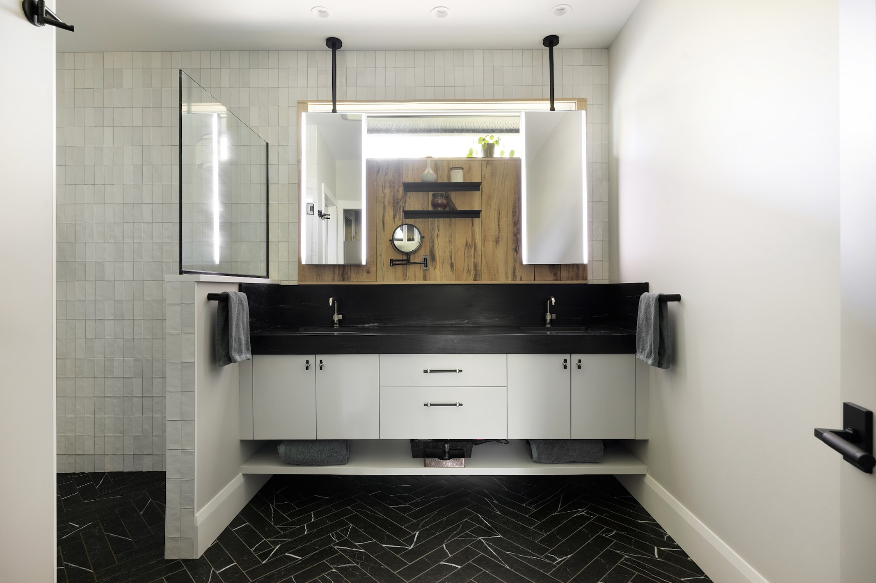 Custom double bathroom vanity with light gray cabinetry, black countertop, integrated open shelf, and wall-mounted mirrors