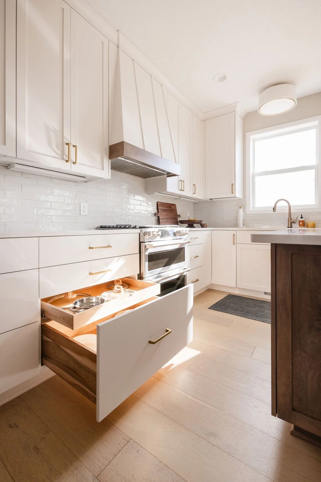 Luxury modern kitchen with white shaker cabinets, brass hardware, light wood floors, stainless steel appliances, and a custom pull-out drawer with integrated pet feeding bowls.