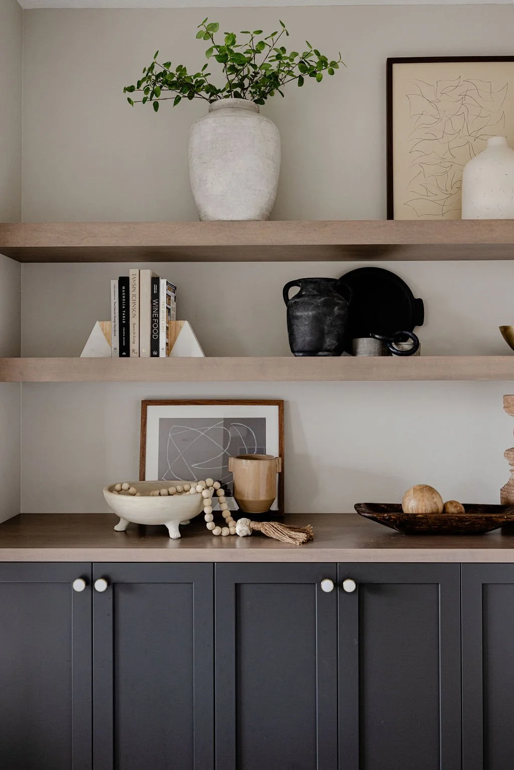 Modern built-in shelves decorated with ceramic vases, books, abstract artwork, and natural wood accents in a neutral living room.