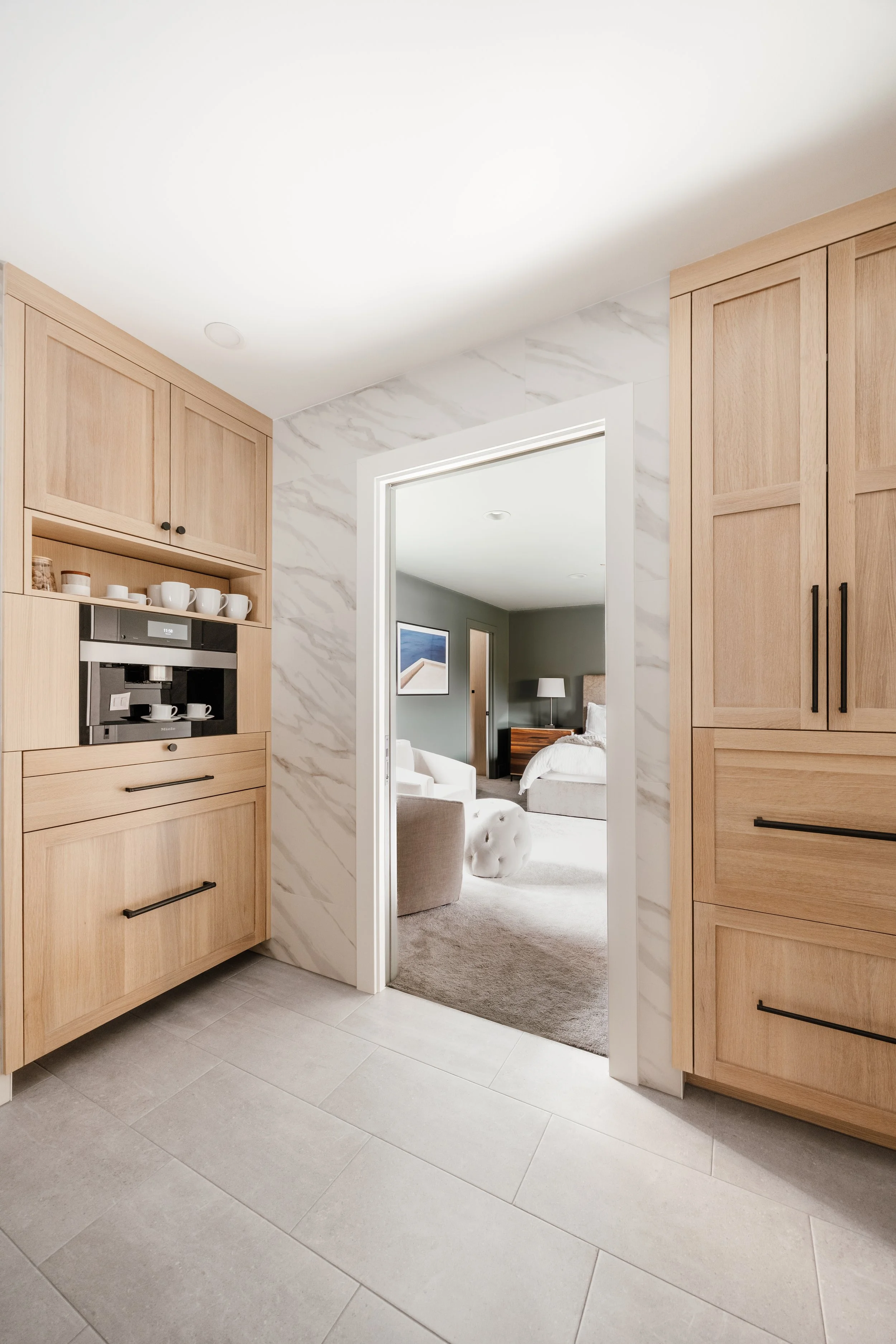 Light wood cabinets with built-in coffee station framing a doorway to a cozy bedroom suite