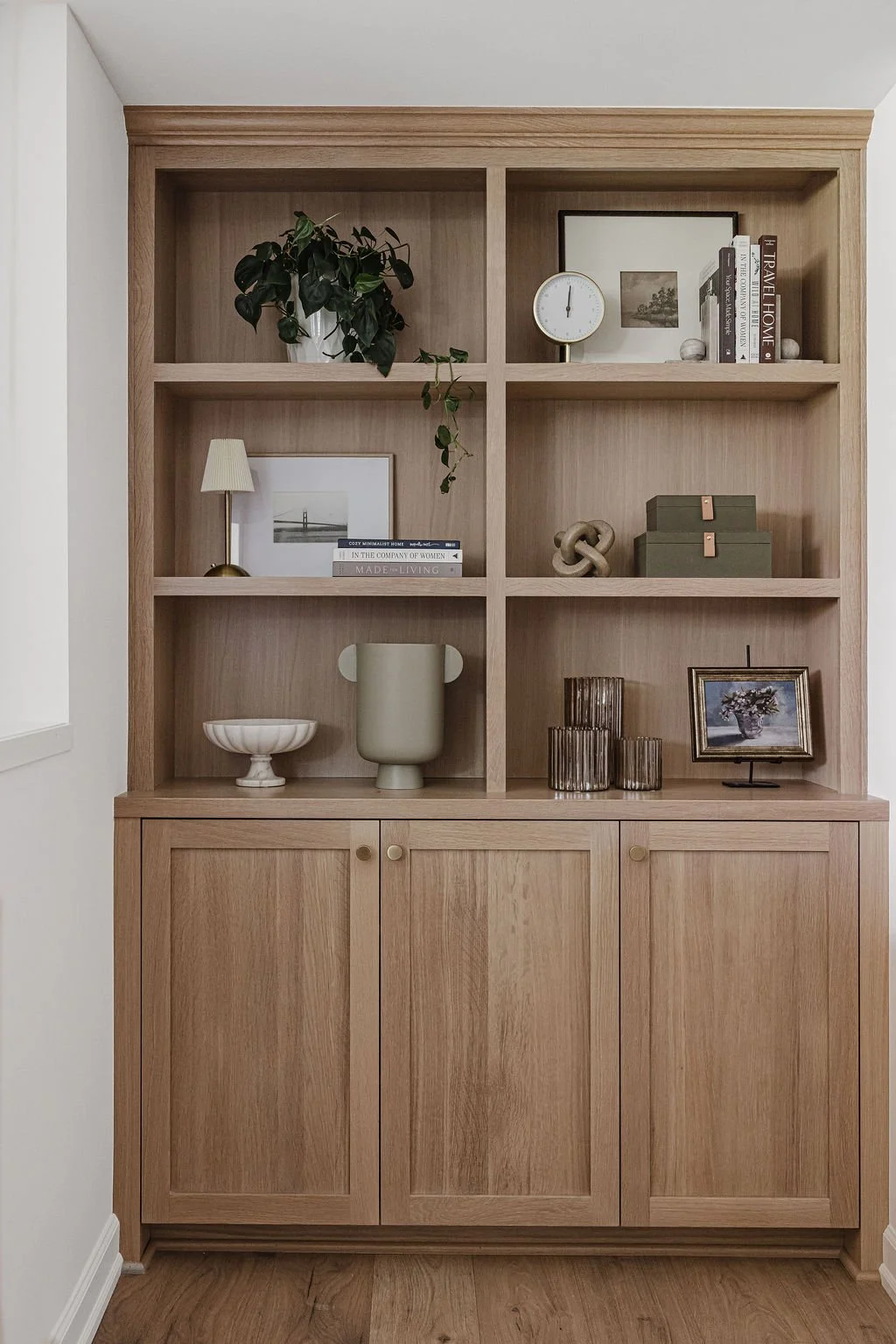 Custom light wood built-in cabinetry with open shelves, styled with books, plants, and modern decorative accessories.