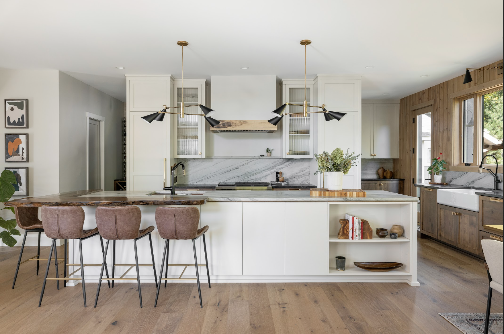 Custom kitchen cabinetry with a large white island, integrated shelving, mixed wood finishes, and modern brass-accent lighting