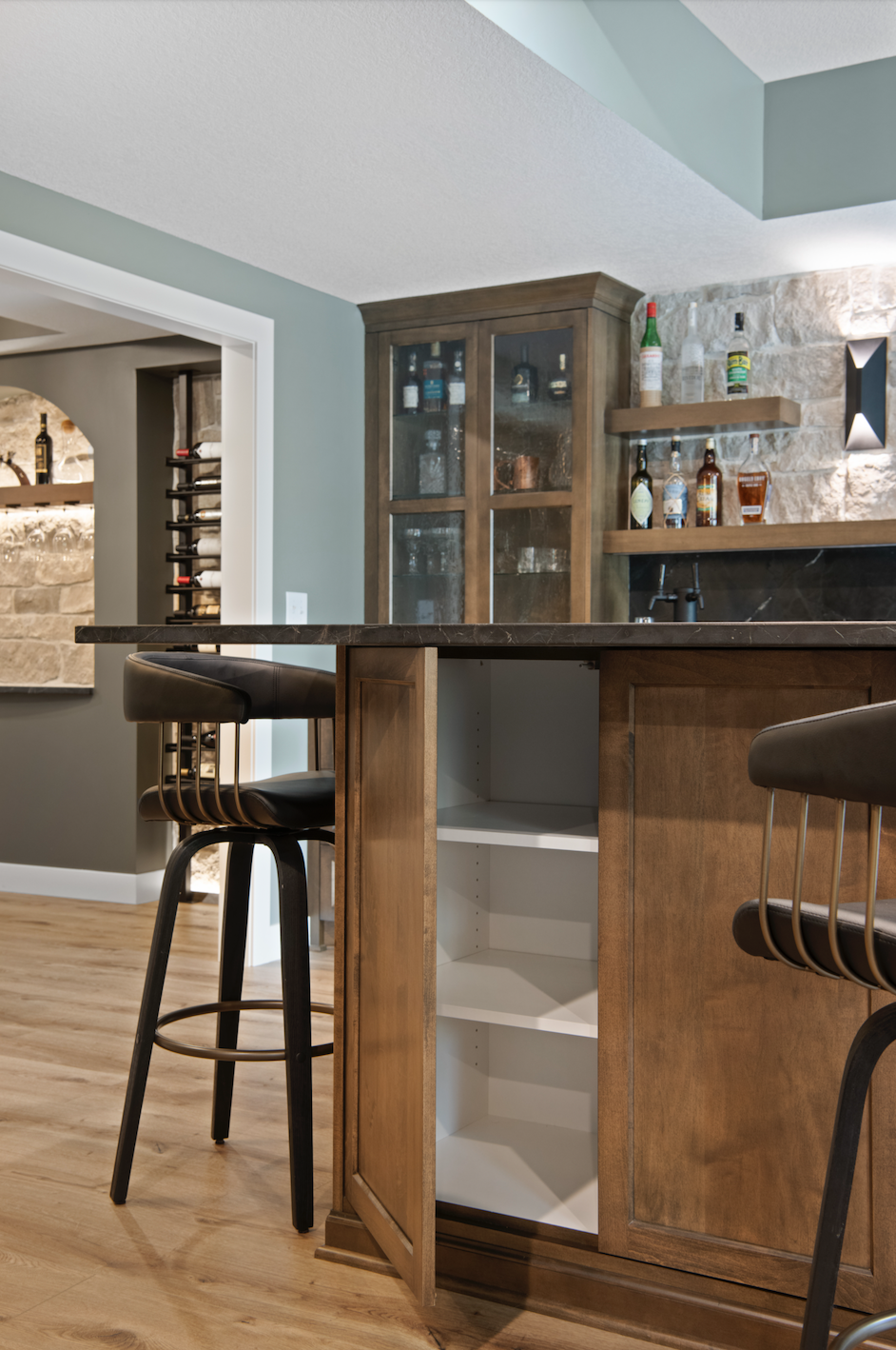 Custom home bar cabinetry with glass-front liquor cabinet, wood drawers with brass hardware, floating shelves, and adjacent temperature-controlled wine storage.