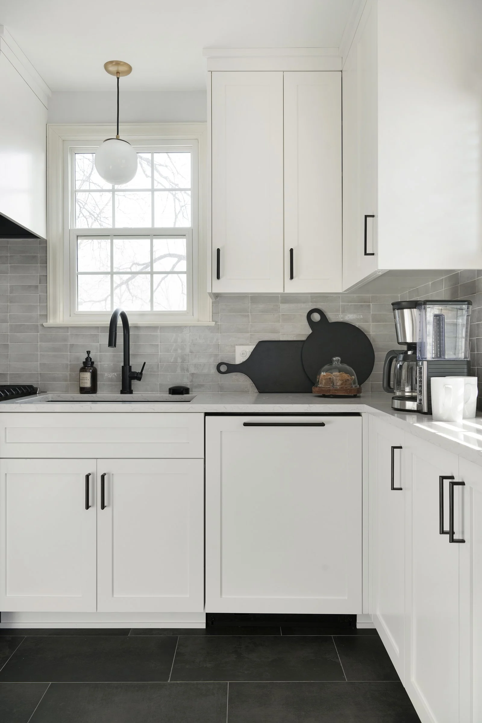 Bright white kitchen with shaker cabinets, black hardware, and a window above the sink.