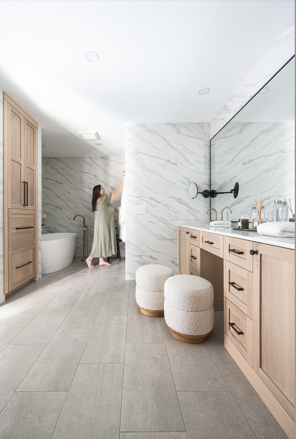 Bright bathroom with light wood cabinets, marble walls, freestanding tub, and double vanity