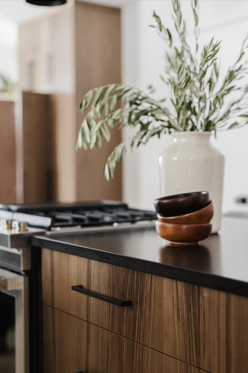 Close-up of a bespoke walnut kitchen island showing an integrated gas range, dark quartz surfaces, and flat-panel drawers with minimalist black hardware.