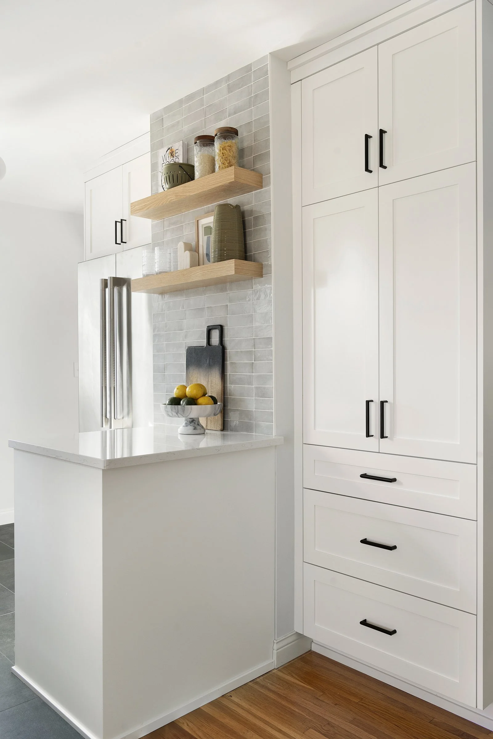 White shaker cabinets with black hardware and open wood shelves beside a built-in refrigerator