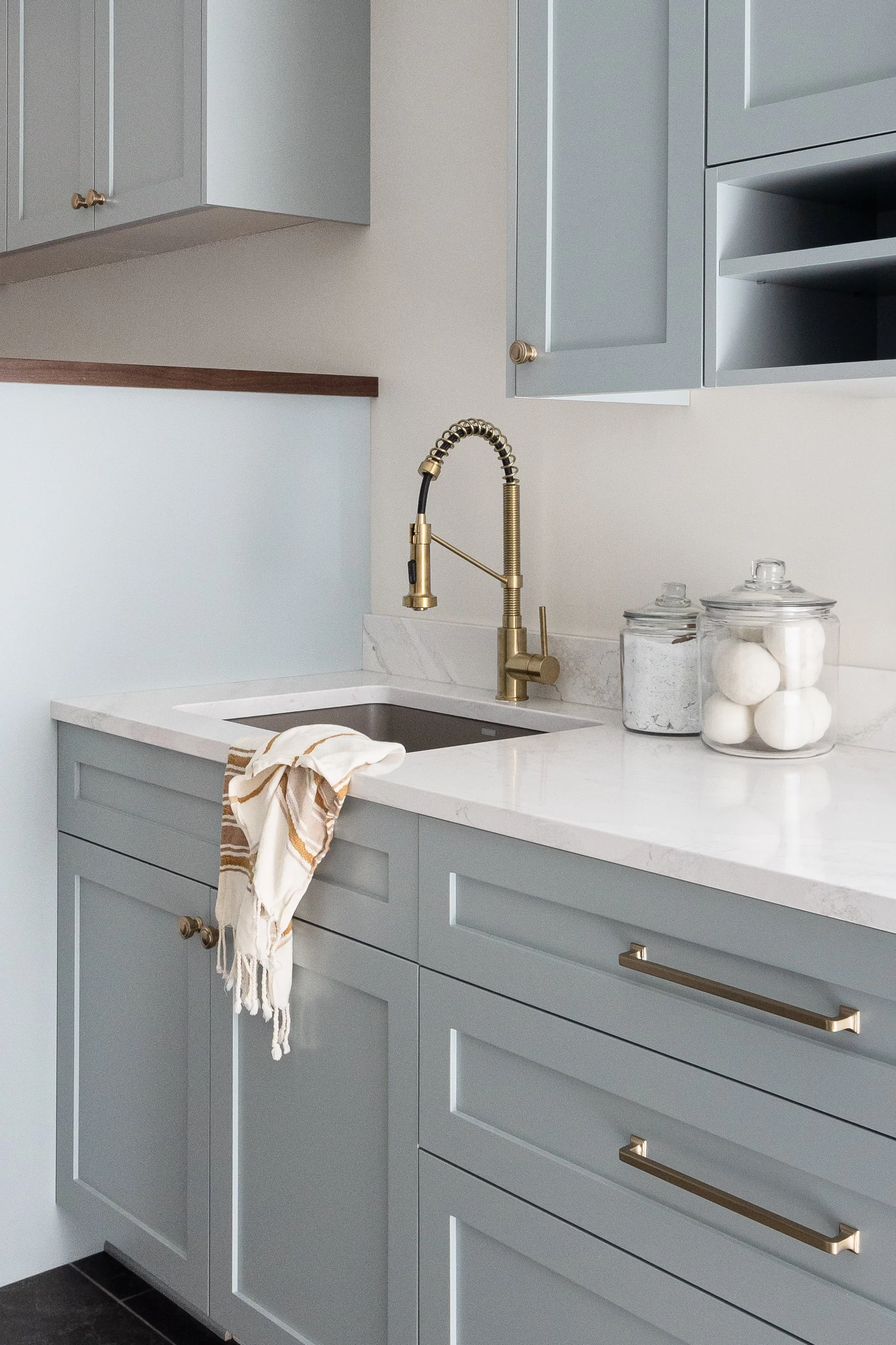Light blue custom shaker cabinets with brass hardware and a quartz countertop in a modern laundry room with a gold pull-down faucet