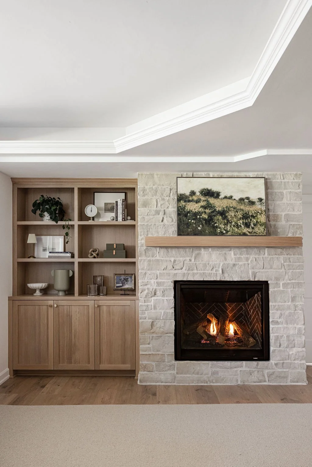 Custom built-in cabinetry in light wood with open shelving and storage cabinets, paired with a white stone fireplace and wood mantel in a modern living room.