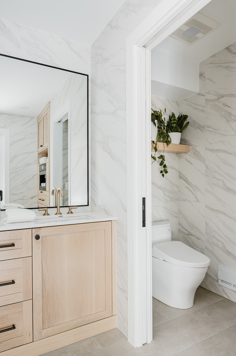 Bathroom vanity with light wood cabinets and adjacent toilet nook