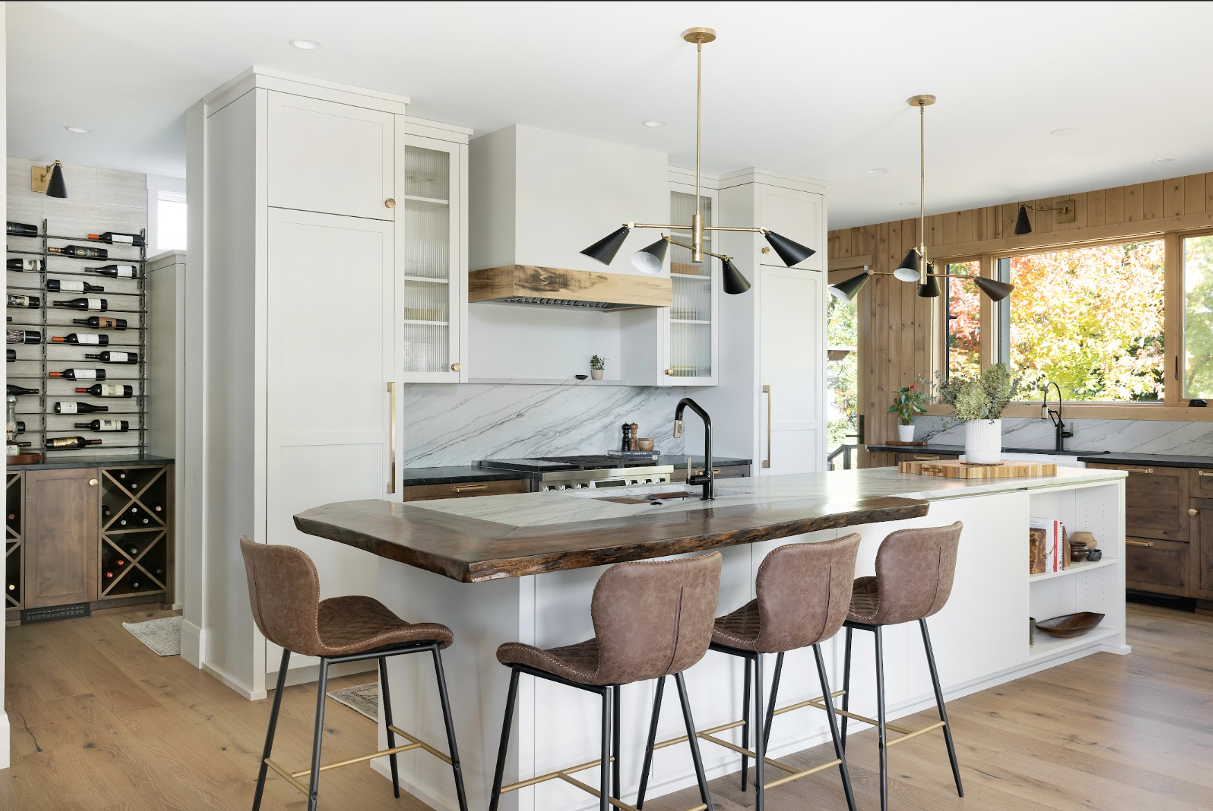 Custom kitchen cabinetry featuring white shaker cabinets, wood accents, marble backsplash, large island, and integrated wine storage.