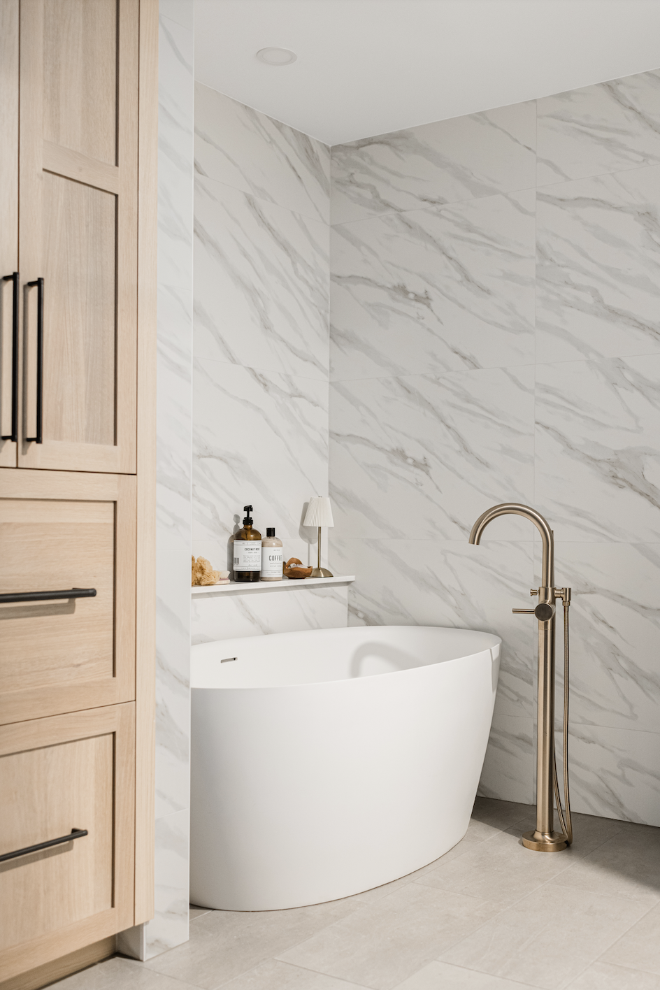 Light wood cabinets next to modern freestanding tub and brass fixture