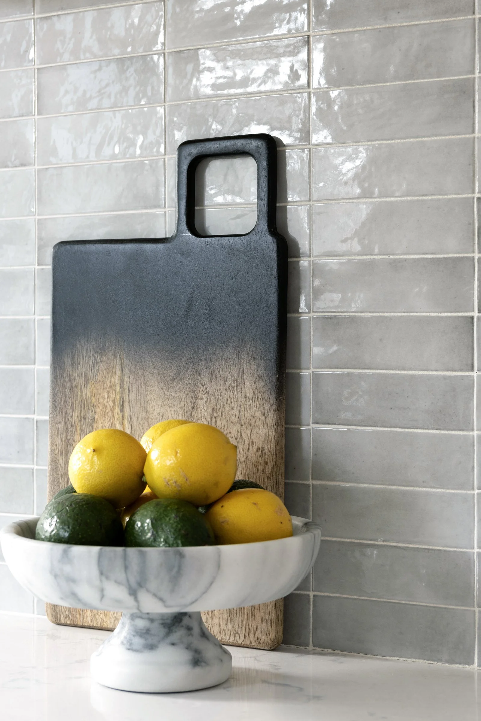 Marble bowl with lemons and limes in front of a gray tile backsplash