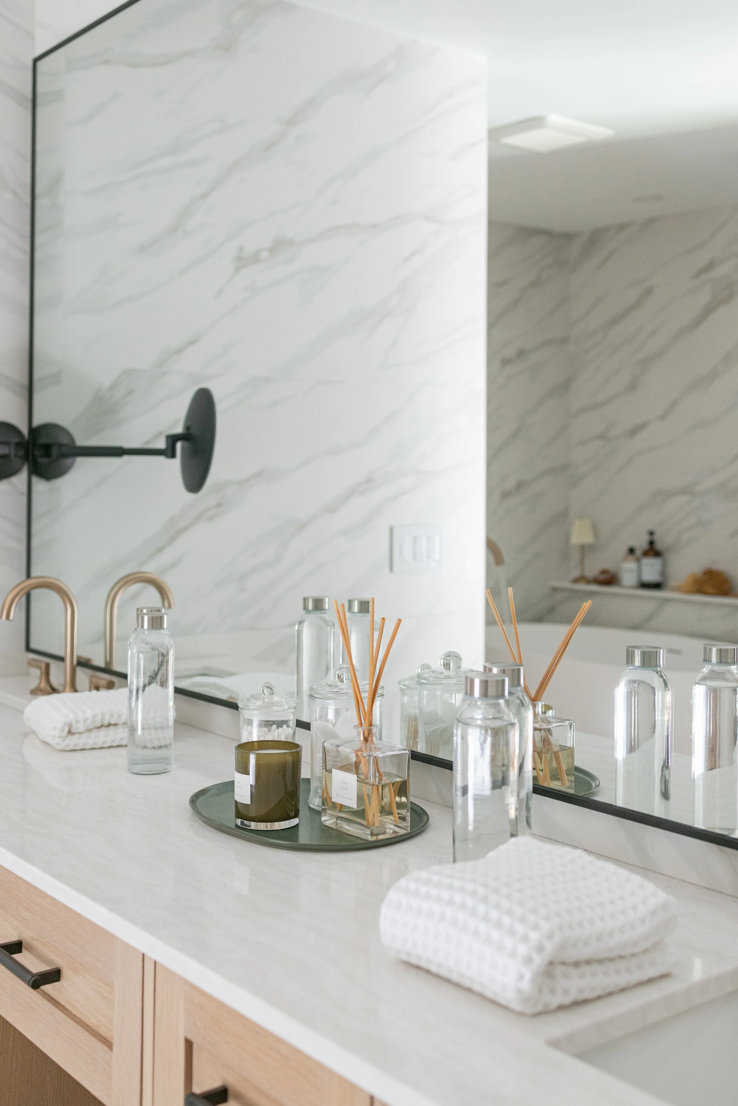 Bathroom vanity cabinets in light wood with marble walls and styled countertop accessories