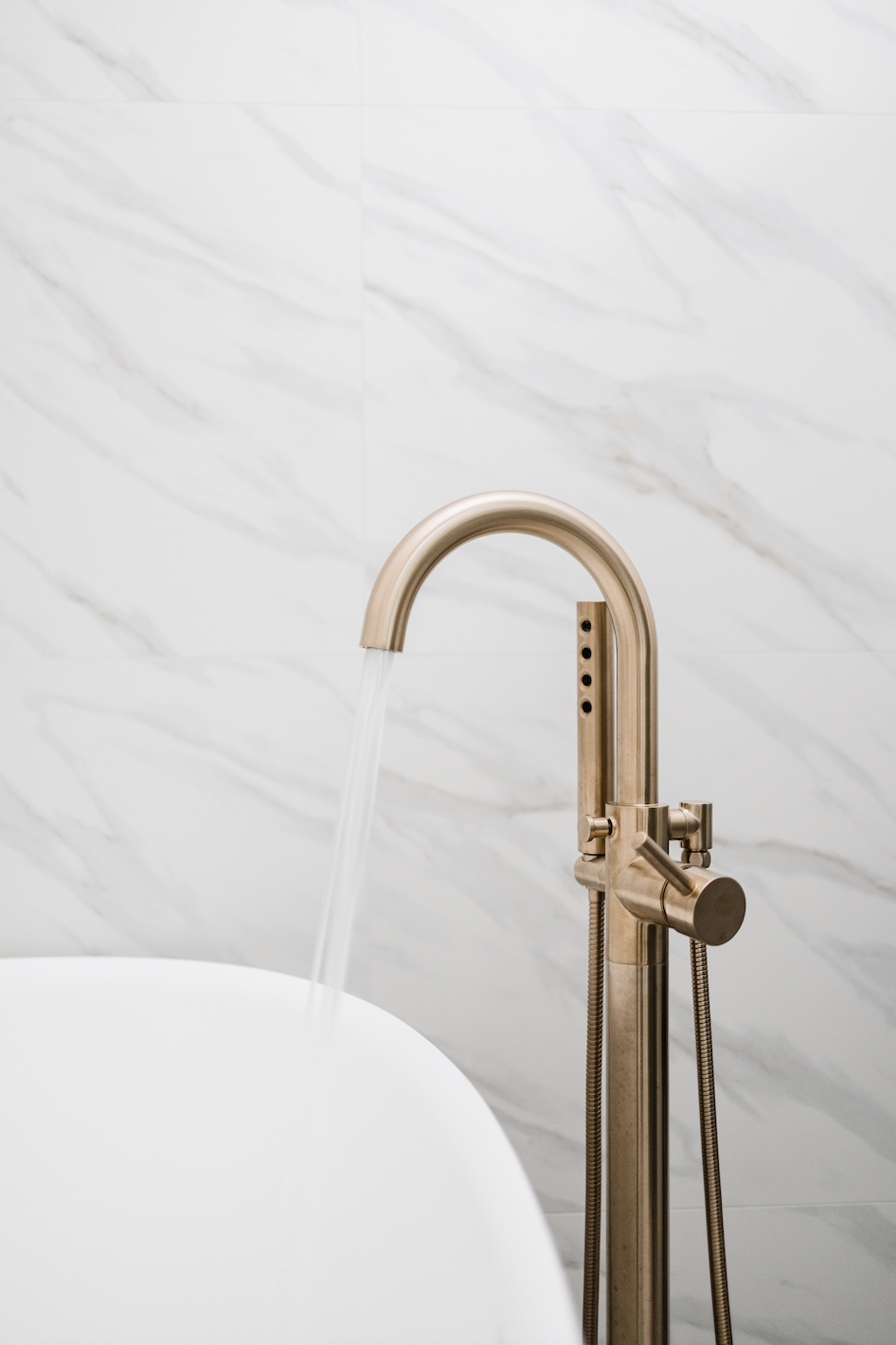 Freestanding tub with brass faucet beside white cabinets
