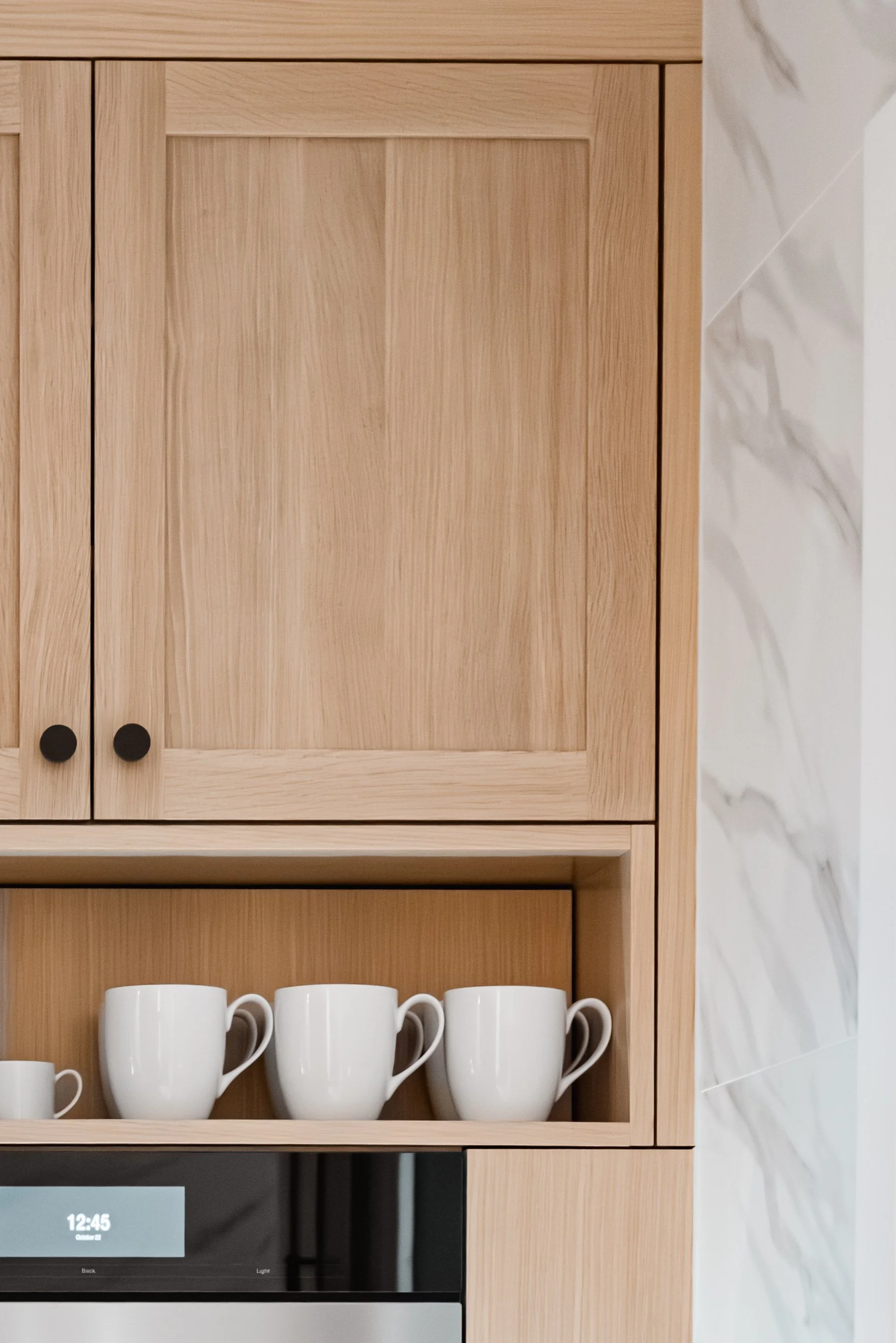 Close-up of light wood cabinets with open shelf displaying white mugs