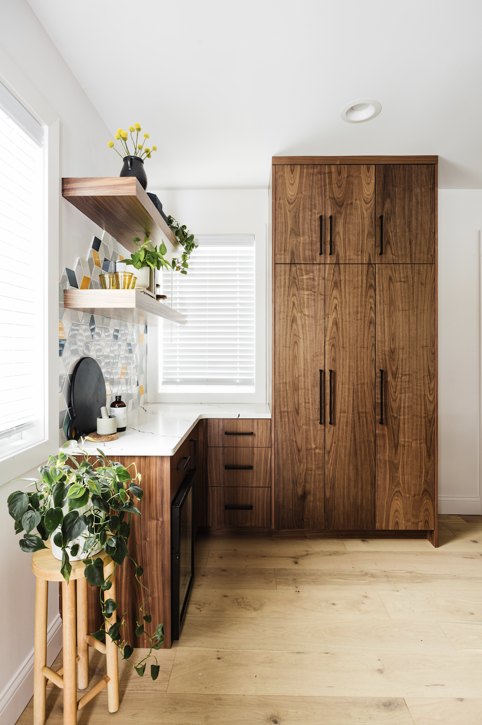 Custom walnut kitchen cabinets with pantry storage, floating shelves, and geometric tile backsplash