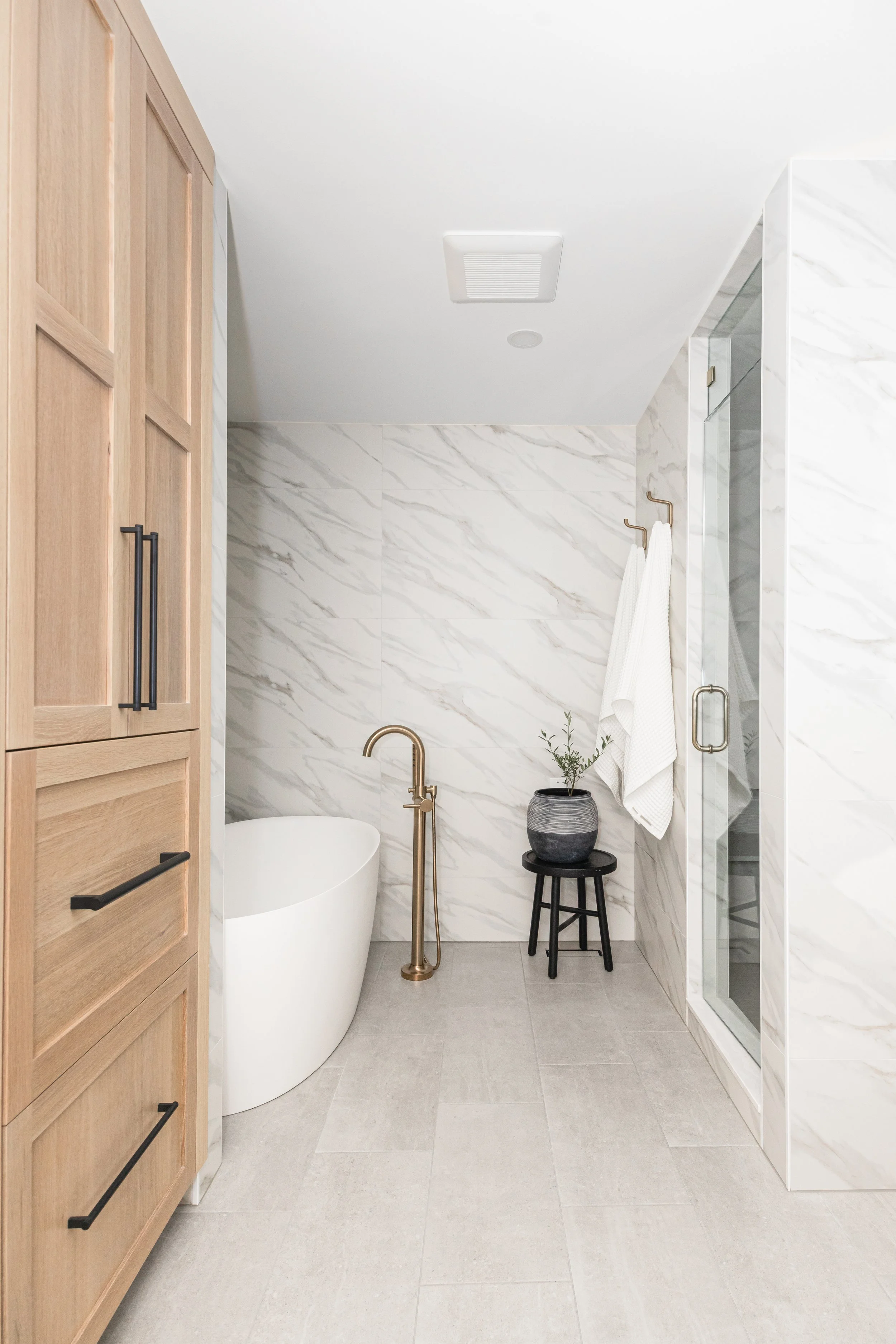Tall light wood cabinets in a modern bathroom with tub and glass shower