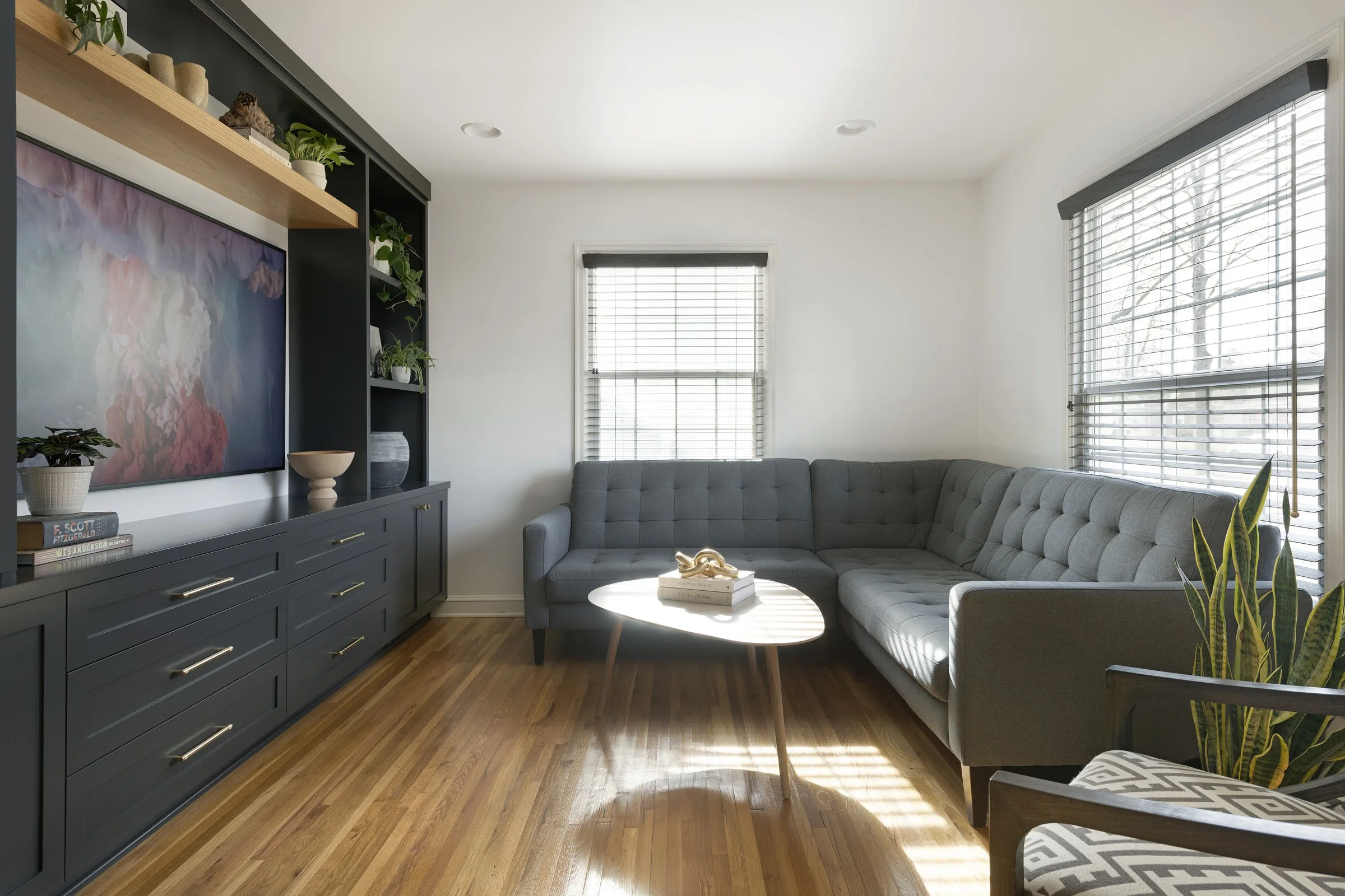 Full view of a modern living room installation featuring floor-to-ceiling black cabinets, integrated TV, and a natural wood floating shelf.