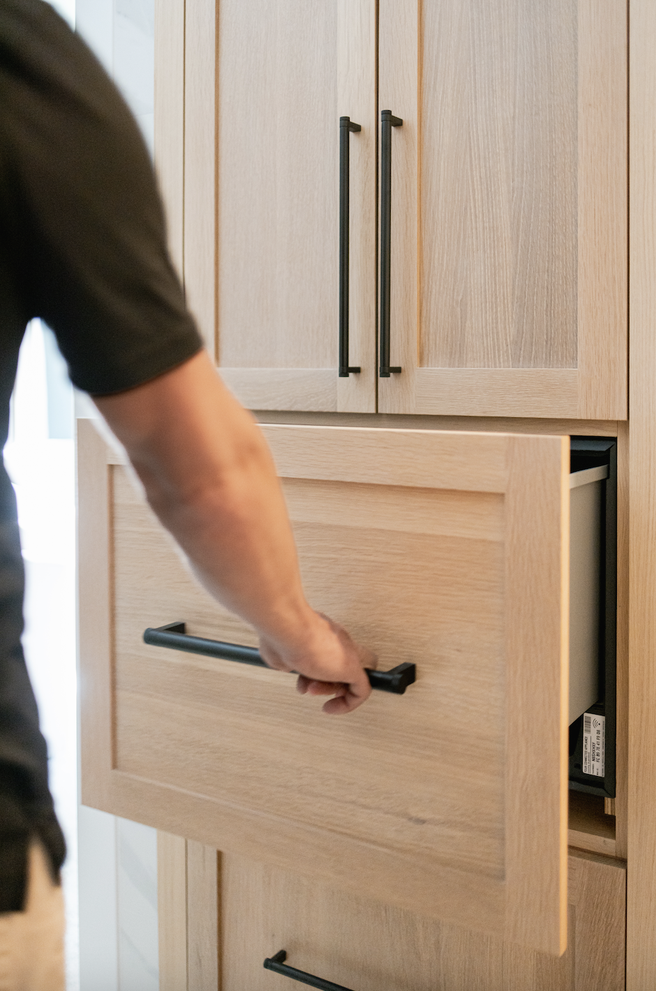 Person opening light wood cabinet drawer with black hardware