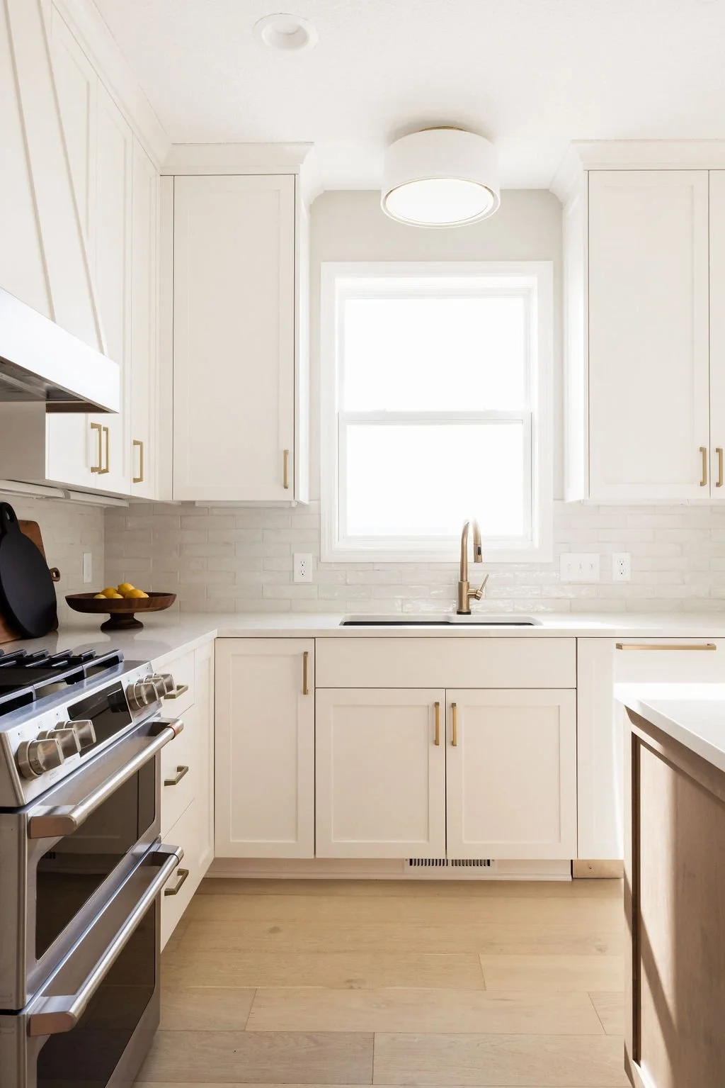 Modern kitchen with custom white shaker cabinets, brass hardware, quartz countertops, and soft-close storage surrounding a stainless-steel range and undermount sink.