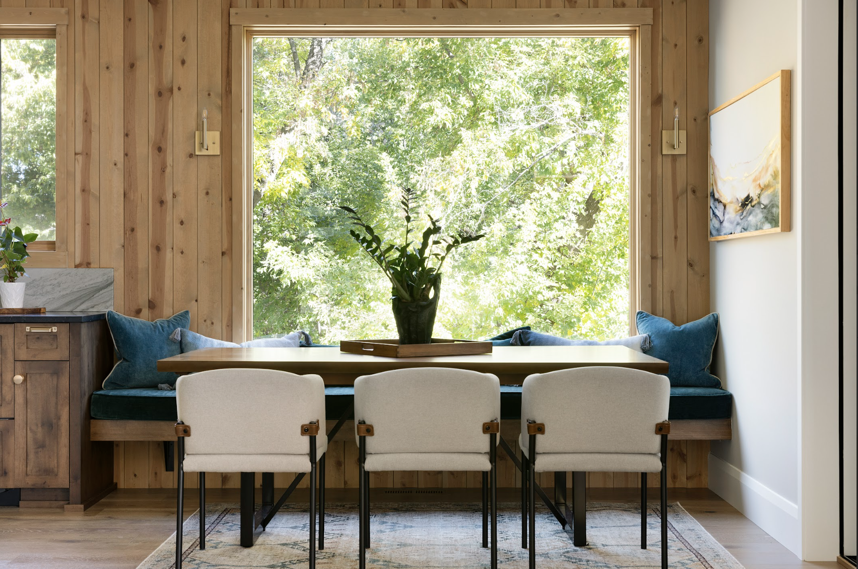 Custom built-in dining nook with wood-paneled walls, integrated bench seating, and a handcrafted wood table positioned beneath a large picture window.