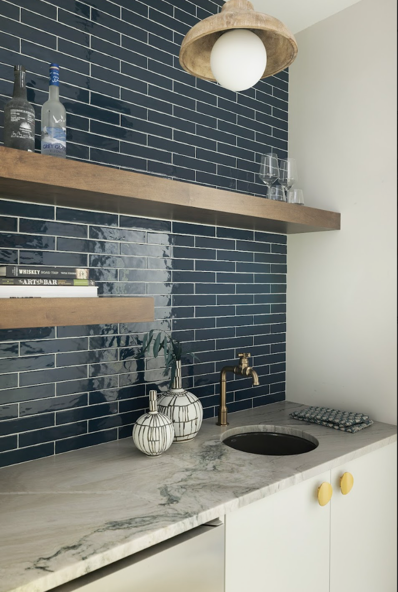 Custom white base cabinets, marble countertop, brass faucet, and floating wood shelves against a dark blue tile backsplash.