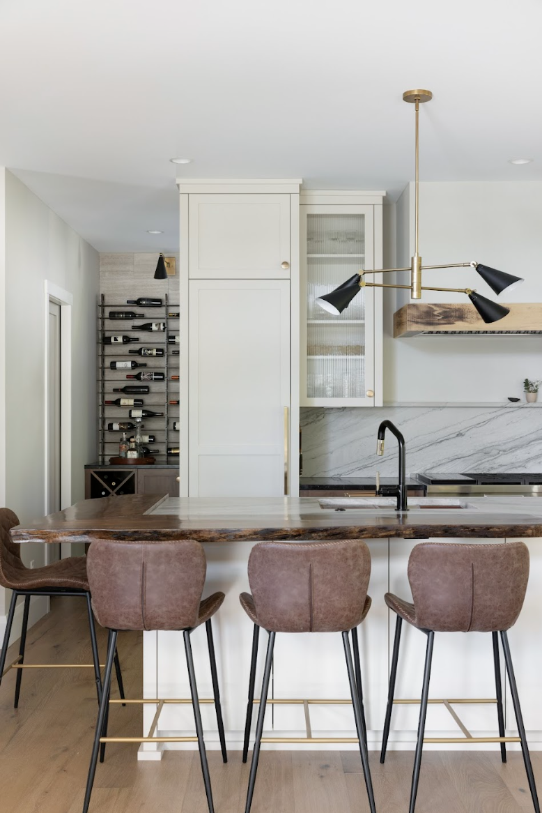 Modern custom kitchen with tall white cabinets, brass hardware, waterfall island seating, and built-in wine rack.