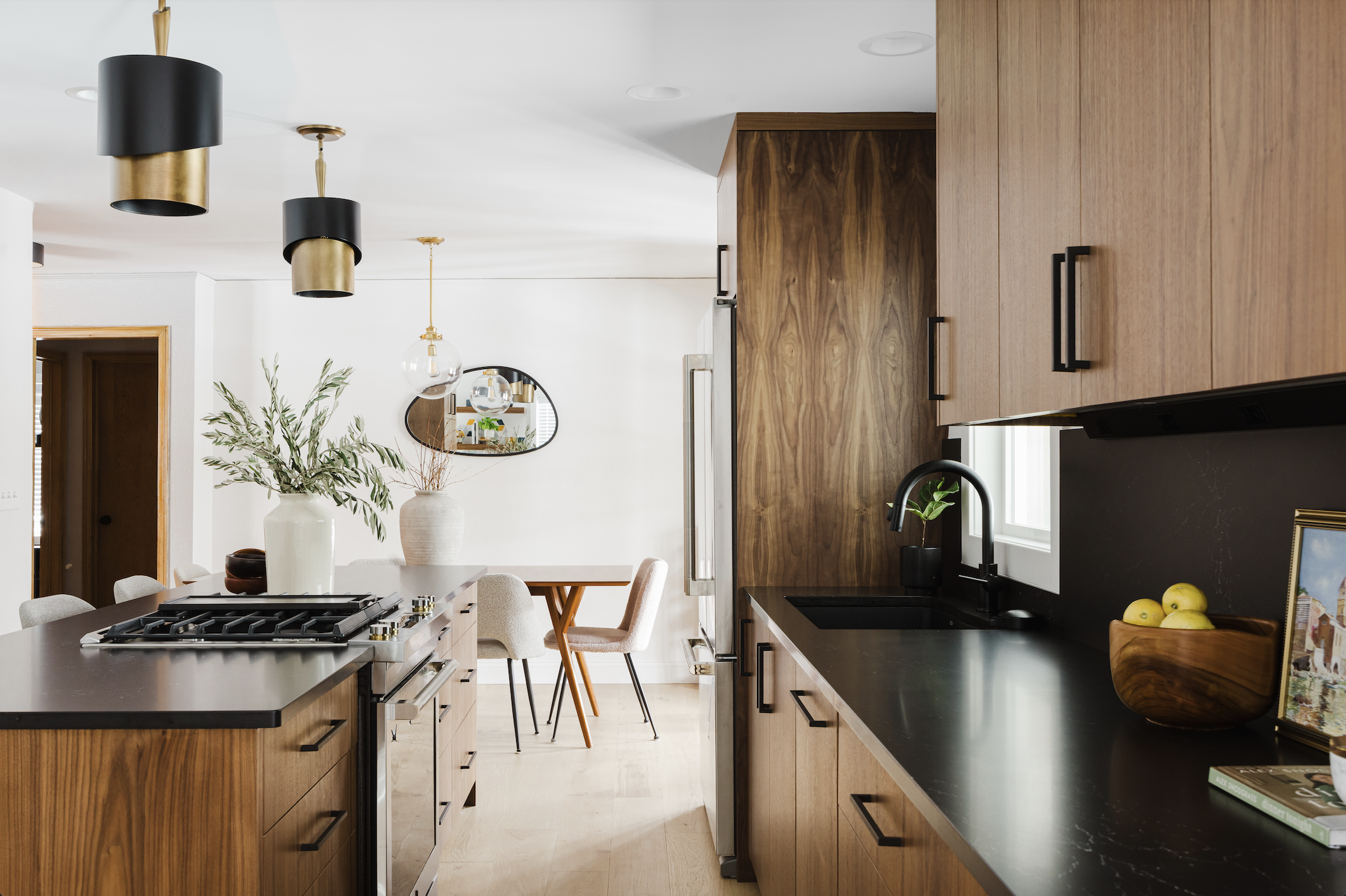 Perspective shot of custom-grain walnut cabinetry and integrated refrigerator panels, highlighting a black quartz island with a stainless steel range and matte black sink fixtures.